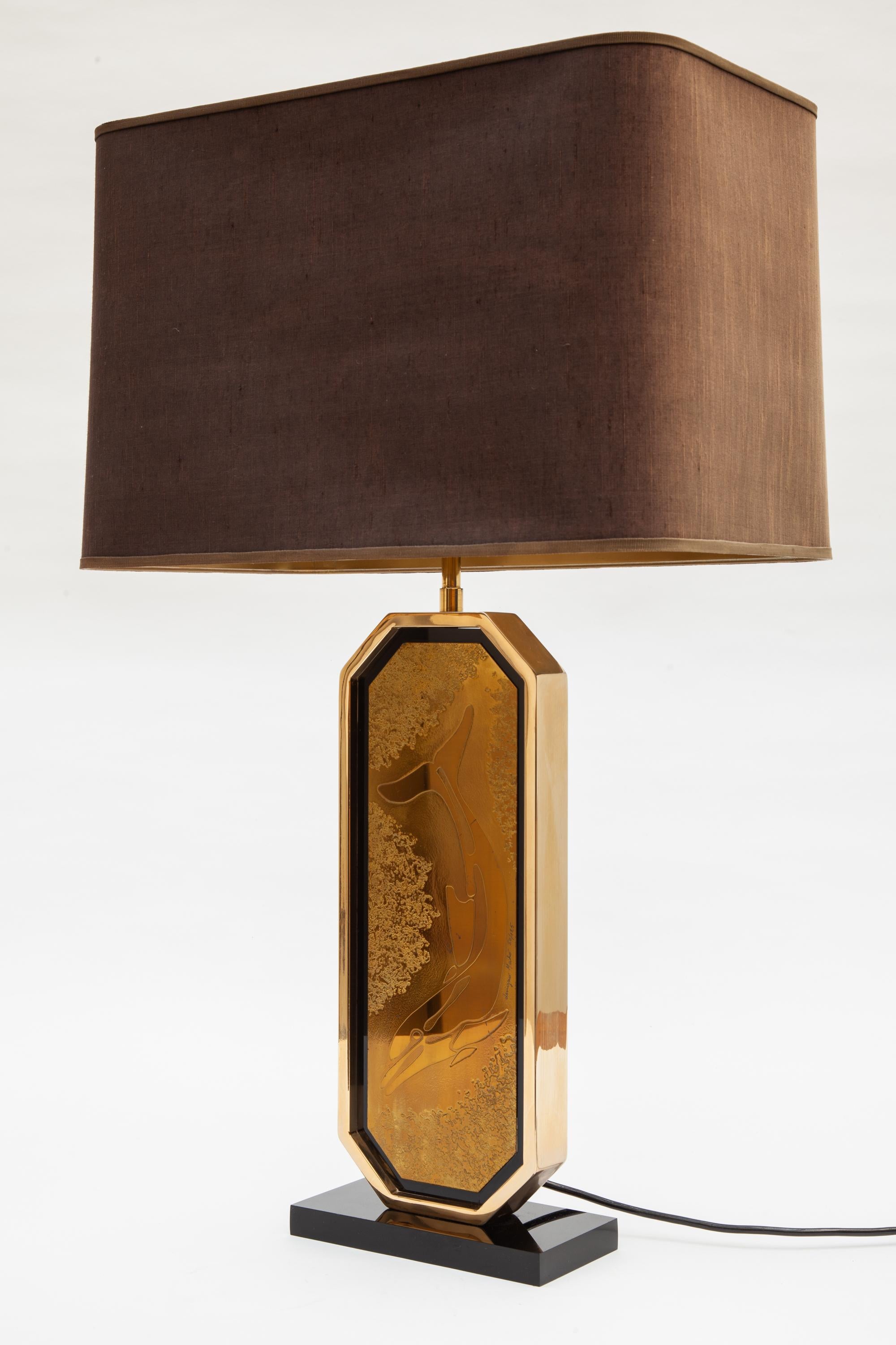 Vintage table lamp by Designo Mahó, Belgium. Gold base with black Lucite accents.
Features a dolphin etching by artist Georges Mathias, signed and numbered 50/125. Raw silk shade with adjustable height. Holds two bulbs.

Measures: 20 W x 9 D x 75