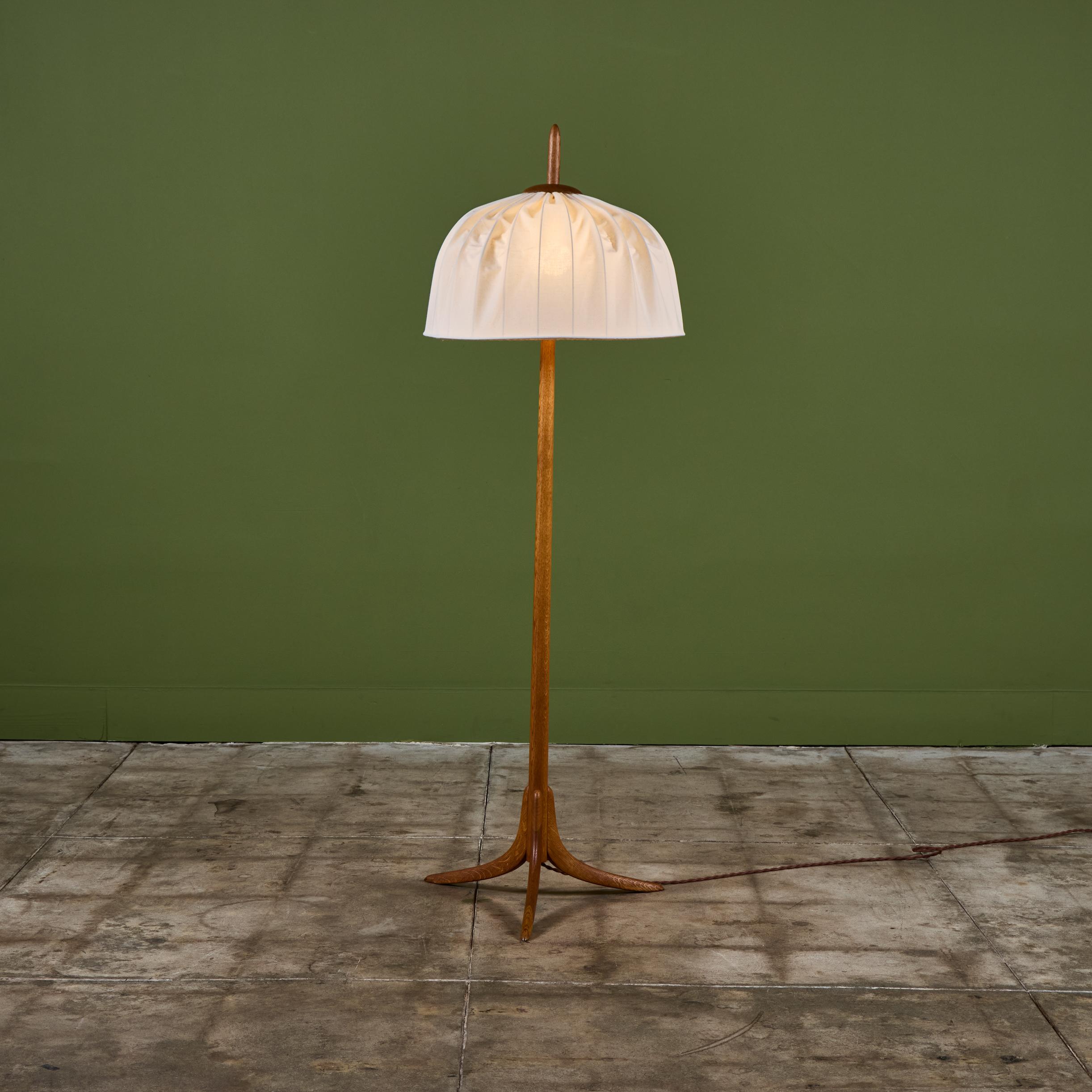 Oak floor lamp with newly upholstered cotton-linen blend shade. The lamp features two light settings for a dimmer or brighter light controlled by two pull chains. The lamp has a narrow oak stem that extends through the top of the lamp and a