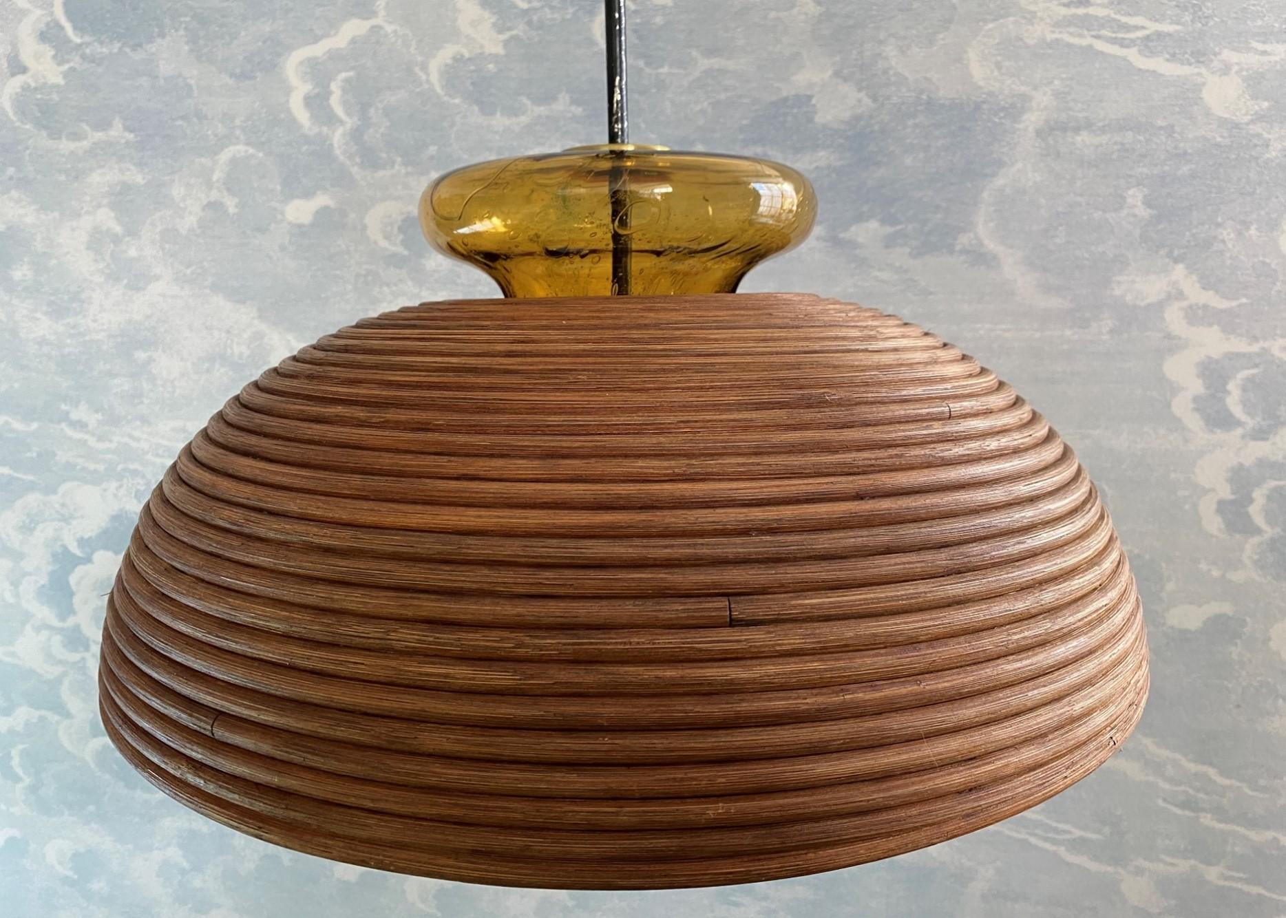 This dome shaped rattan pencil reed pendant lamp with brass accent and topped with an amber glass crown was most likely produced by Vivai Del Sud in Italy in the 1960s.

This extra handblown glass fitting not only adds to the ambient light produced