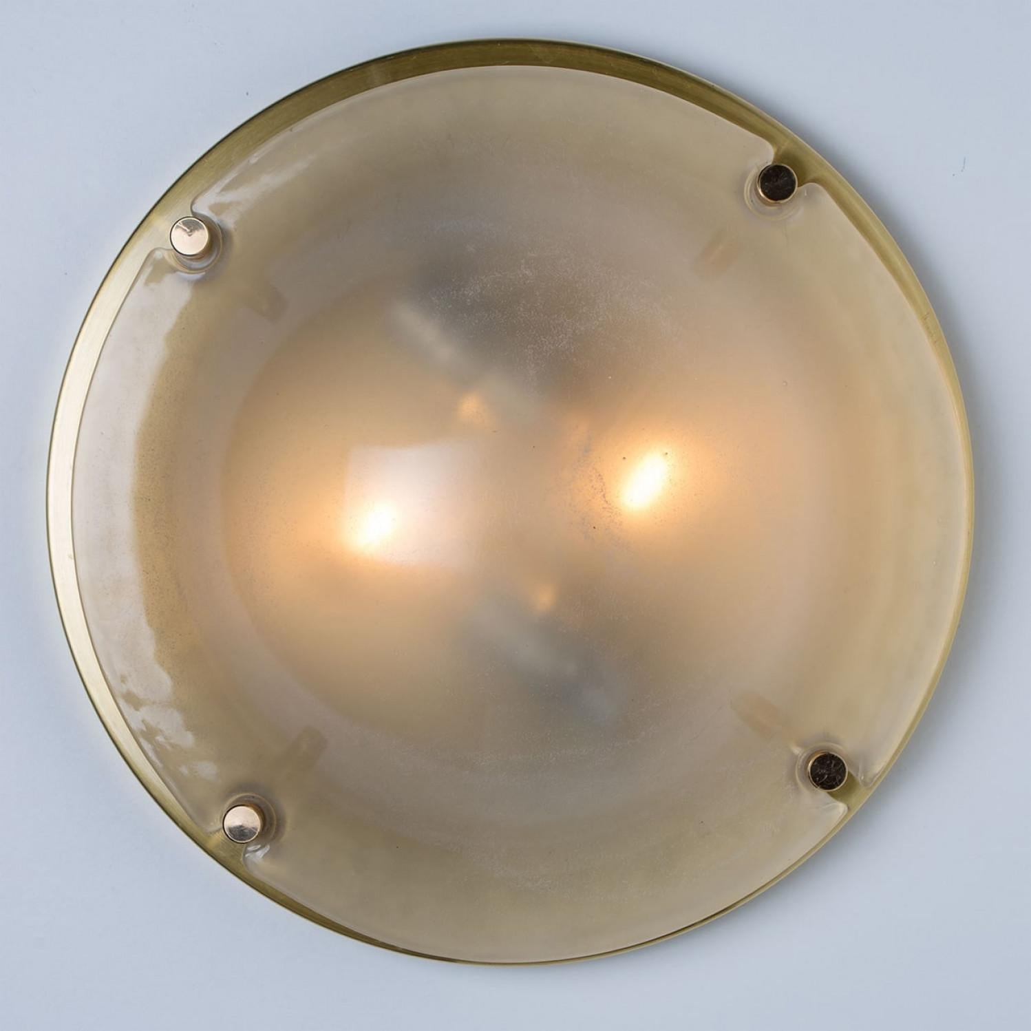 A  stunning high-end brass and frosted glass flushmount manufactured in the late 1960s-early 1970s. The brass ring holds a large heavy blown glass with four brass screws. The frosted glass has a beautiful textured structure. Beautiful craftsmanship