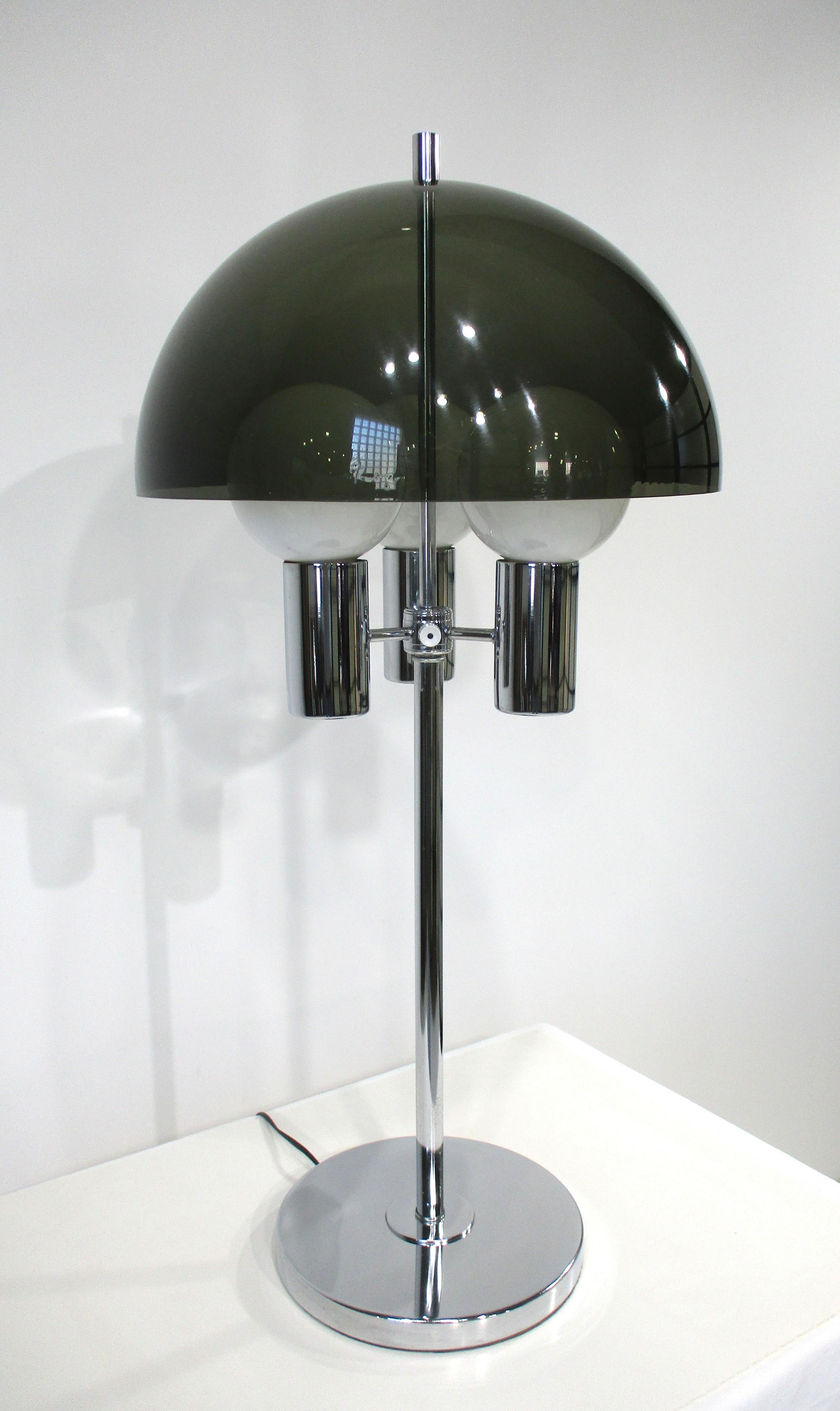 A Space Age styled table lamp with three sockets topped with a smoked darker toned plastic Lucite domed mushroom shade . The shaft and the 10