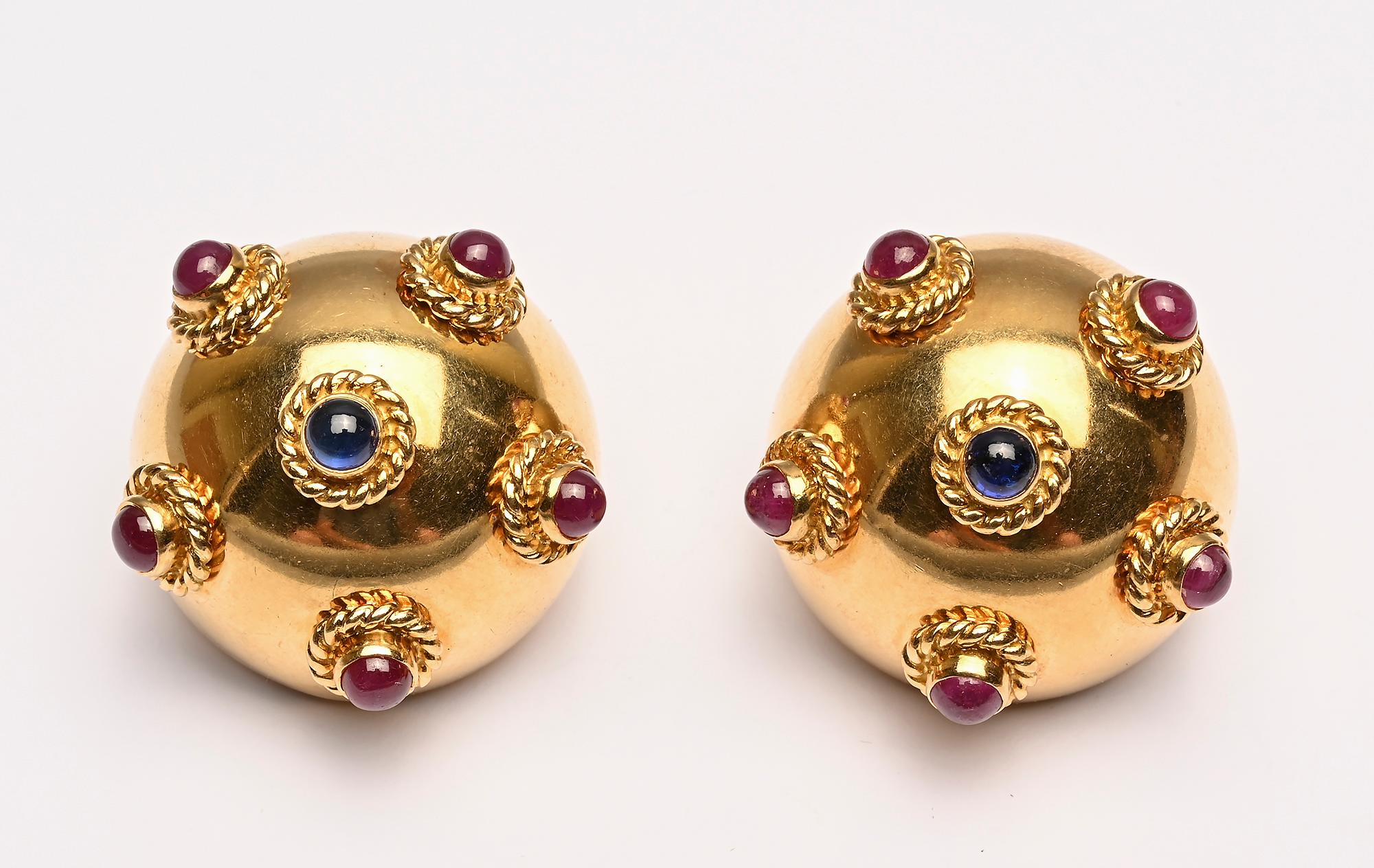 Eighteen karat gold domed earrings centered with a cabochon sapphire and each surrounded by 5 rubies. All of the stones are set in collar bezels surrounded by twisted god. 
Clip backs can be converted to posts. The earrings are 1 1/16