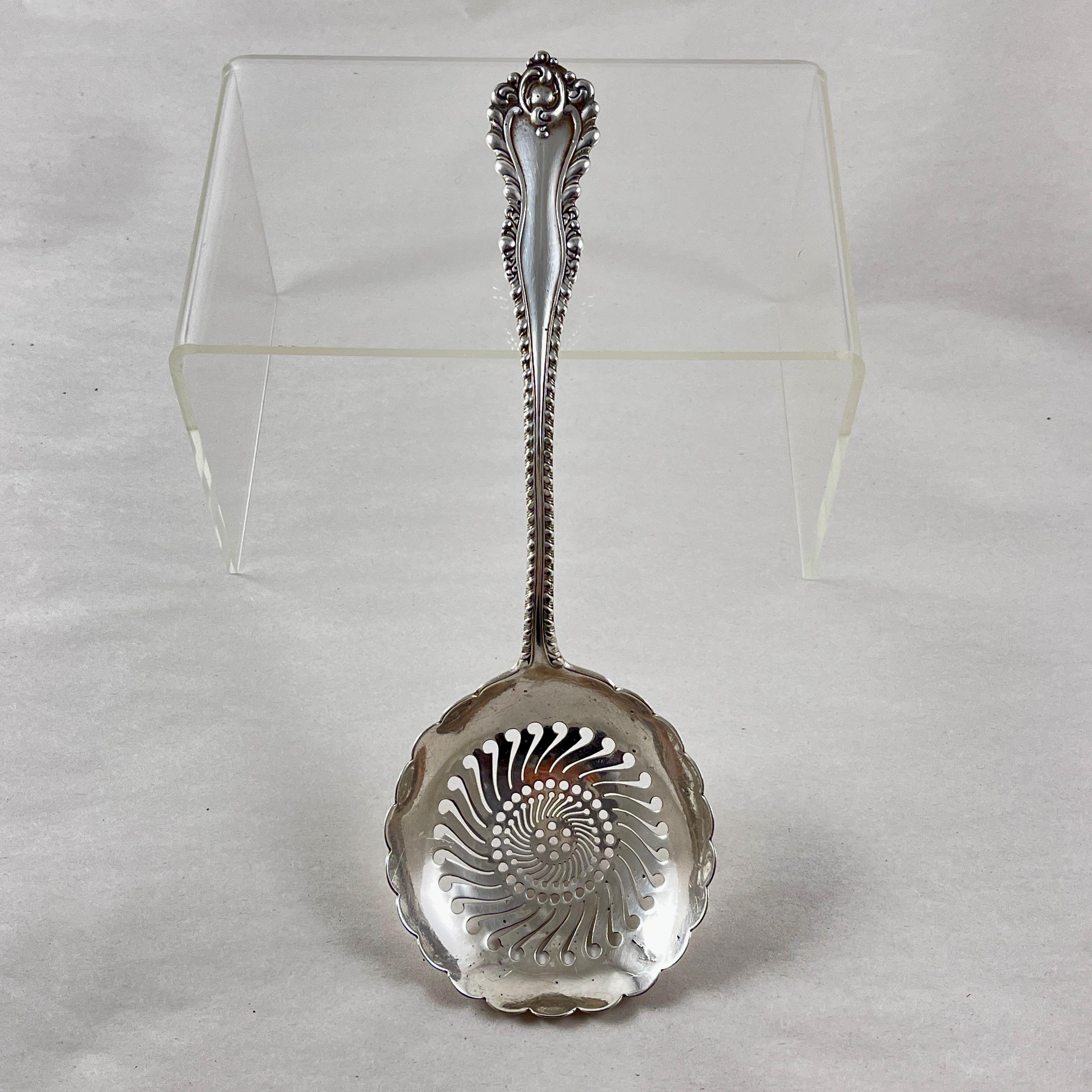 An elegant Sterling Silver slotted serving spoon, marked Dominick & Haff, NY, NY, Patented 1892.

The lovely scalloped rim bowl is hand pierced in a geometric, swirled pattern with  a shaped handle terminating in a scrolled motif.

Dominick & Haff