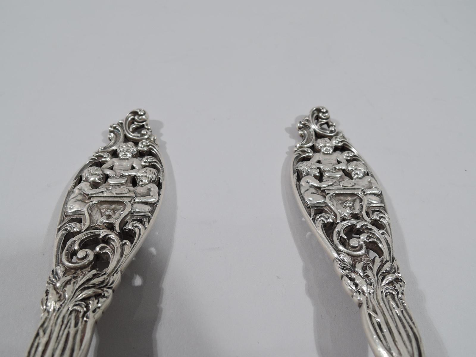 Labors of Cupid sterling silver salad servers. Made by Dominick & Haff in New York, circa 1900. This set comprises spoon and fork. Each stem scrolled and shaped with leaf and flower. Each terminal scrolled and pierced, and inset with 3 chubby