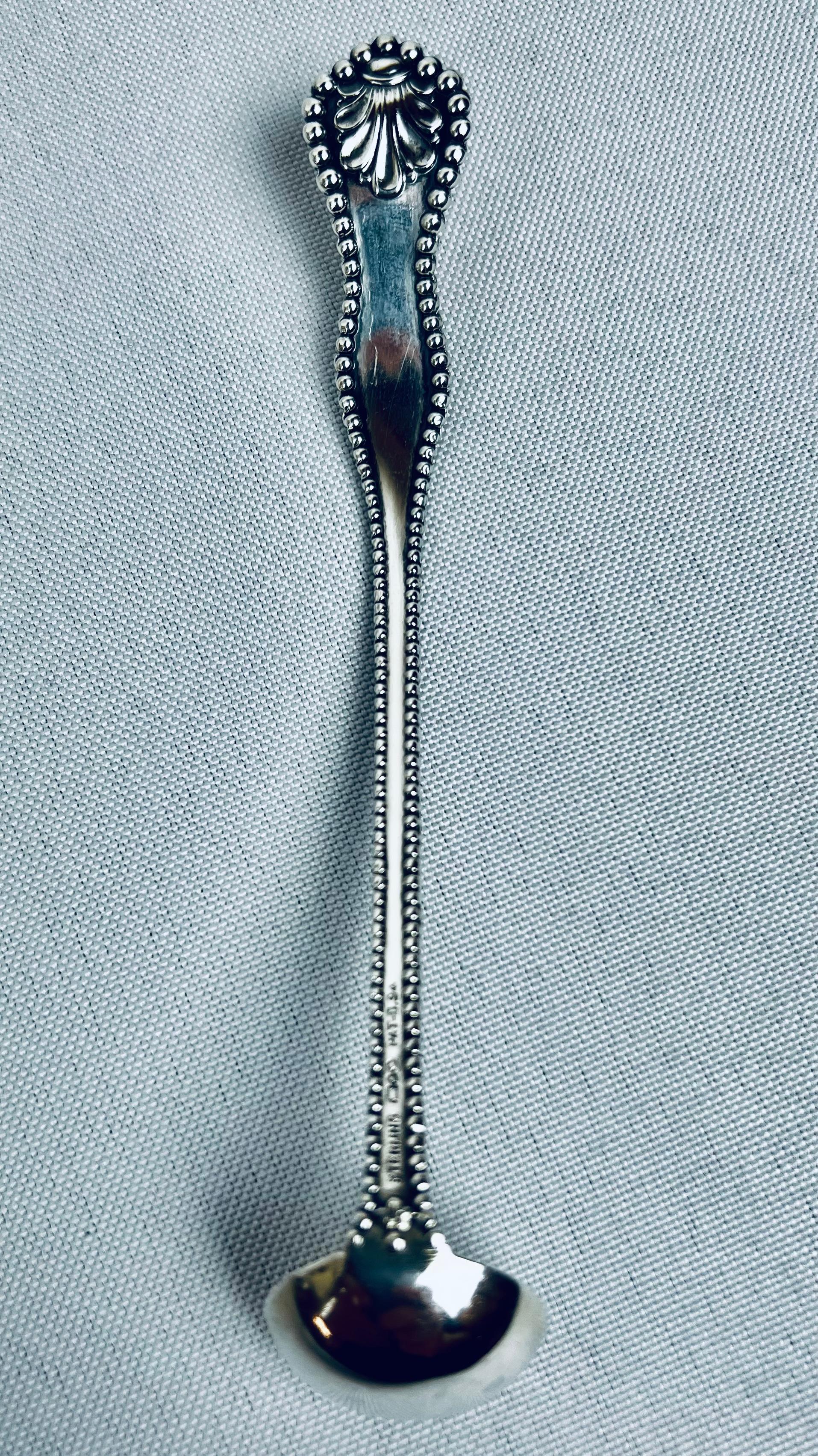 Mestolo per condimenti o senape in argento sterling con bordo in rilievo davanti e dietro.  Il motivo della conchiglia si trova nella parte superiore del cucchiaio, sia davanti che dietro.
Il rovescio è interamente stampato in sterling con i marchi