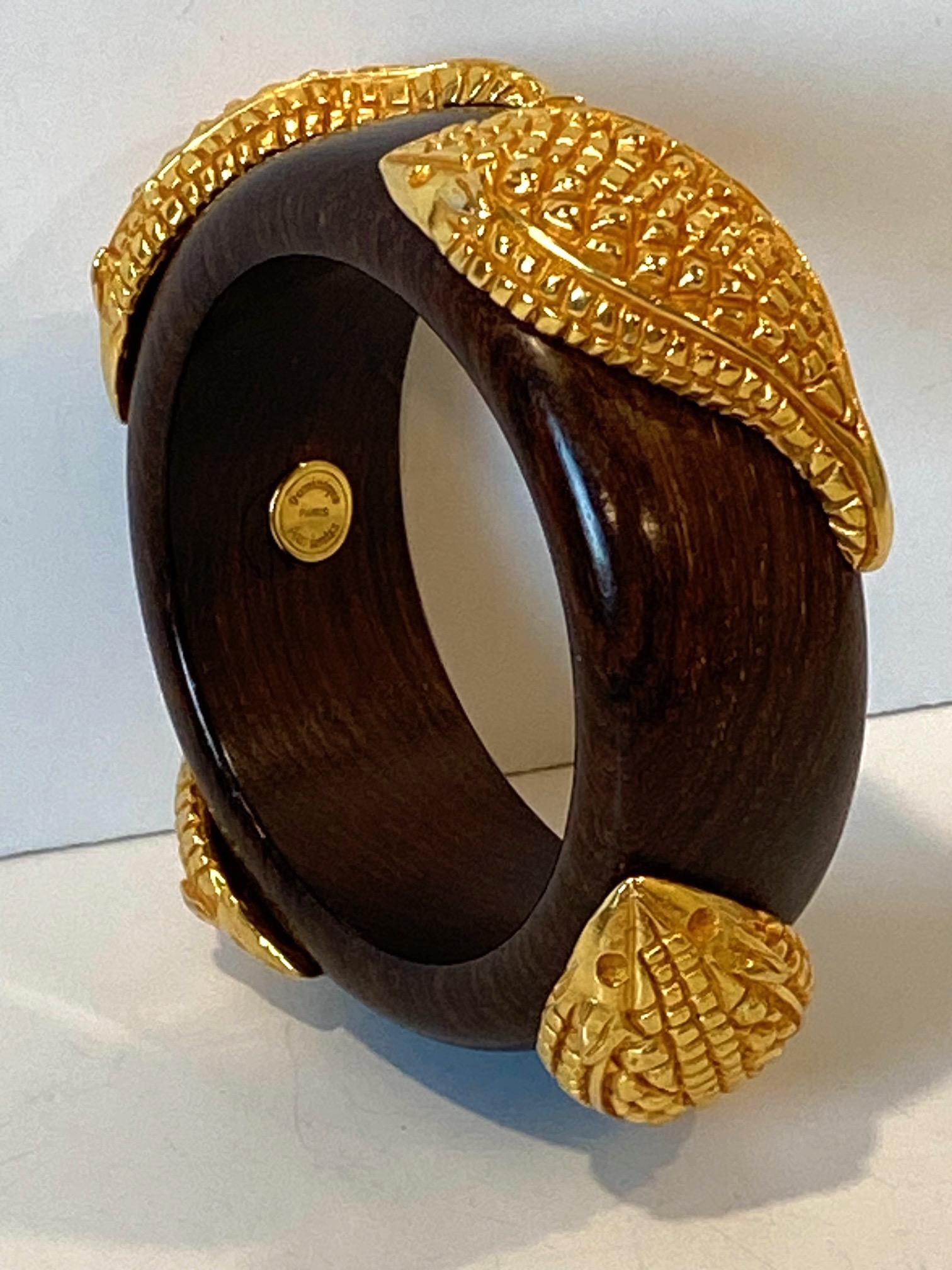 Featured is a wonderful 1980s wood and gilt bangle bracelet by French fashion designer Dominique Aurientis of Paris. She founded her namesake accessory and fashion jewelry brand in 1986. This bracelet is comprised of a 3.25 inch wide dark wood
