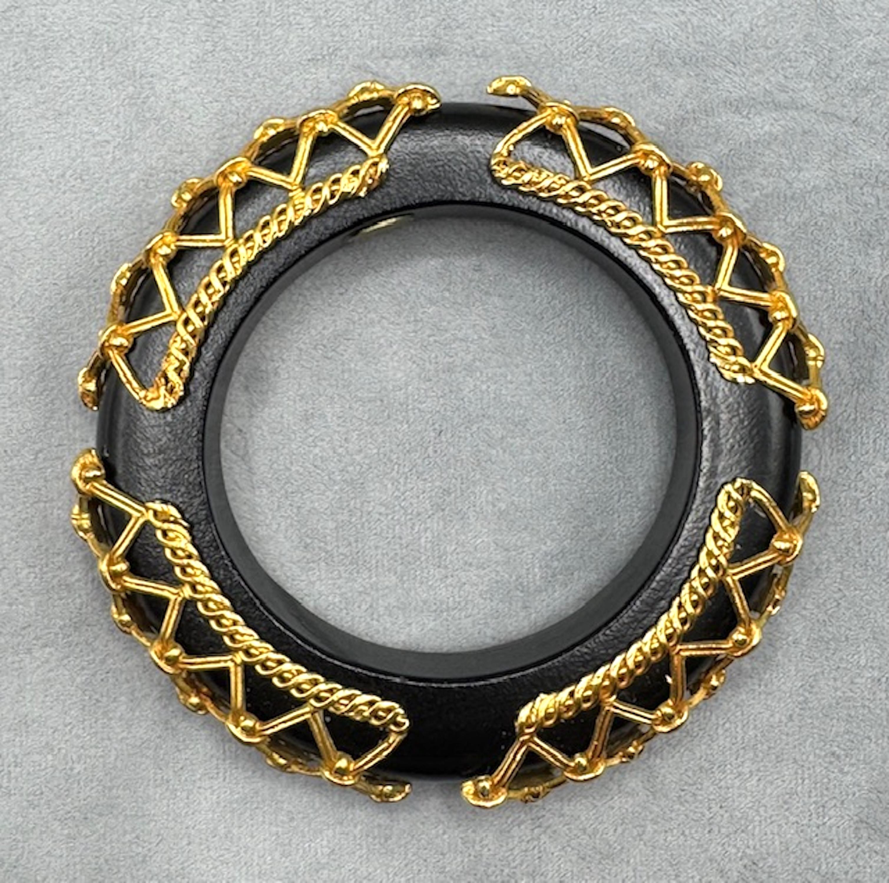 This striking vintage bangle by French designer Dominique Aurientis showcases her signature blend of bold form and opulent detailing. Crafted from rich, black-lacquered wood, the wide bracelet is adorned with intricate, crisscrossed gold-tone