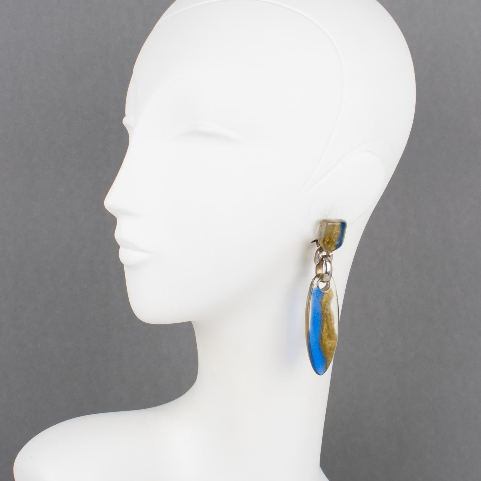 Dominique Denaive Paris designed these elegant resin clip-on earrings. The dangling shape boasts an elongated drop in a lovely semi-transparent color with cobalt blue and pearlized gold inclusions. Silver plate metal hardware linked the fastenings