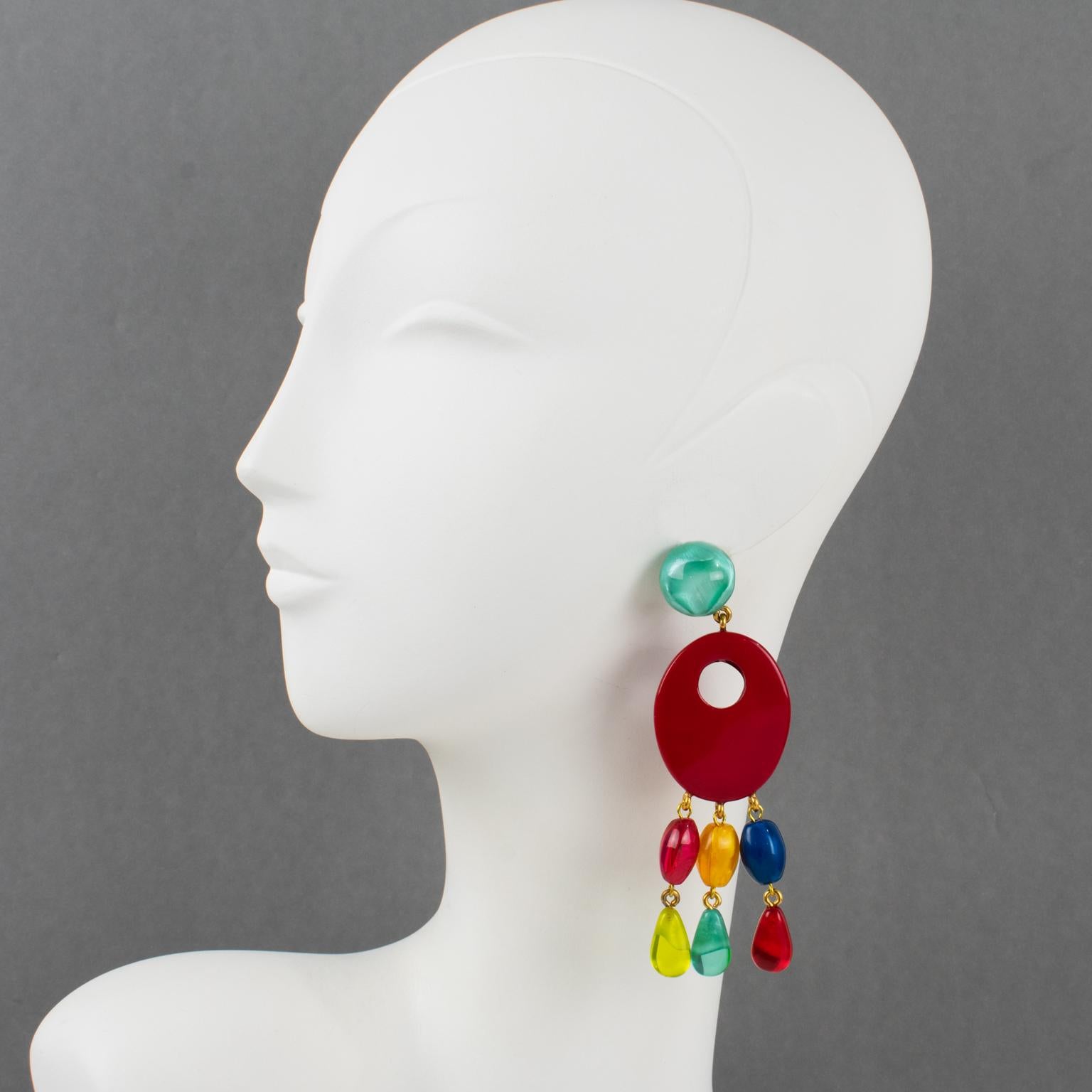 These stunning oversized pierced earrings by Dominique Denaive Paris feature a sculptural chandelier dangling shape. The carved and see-thru oval resin elements are embellished with teardrop charms. The solid bright red color contrasts with
