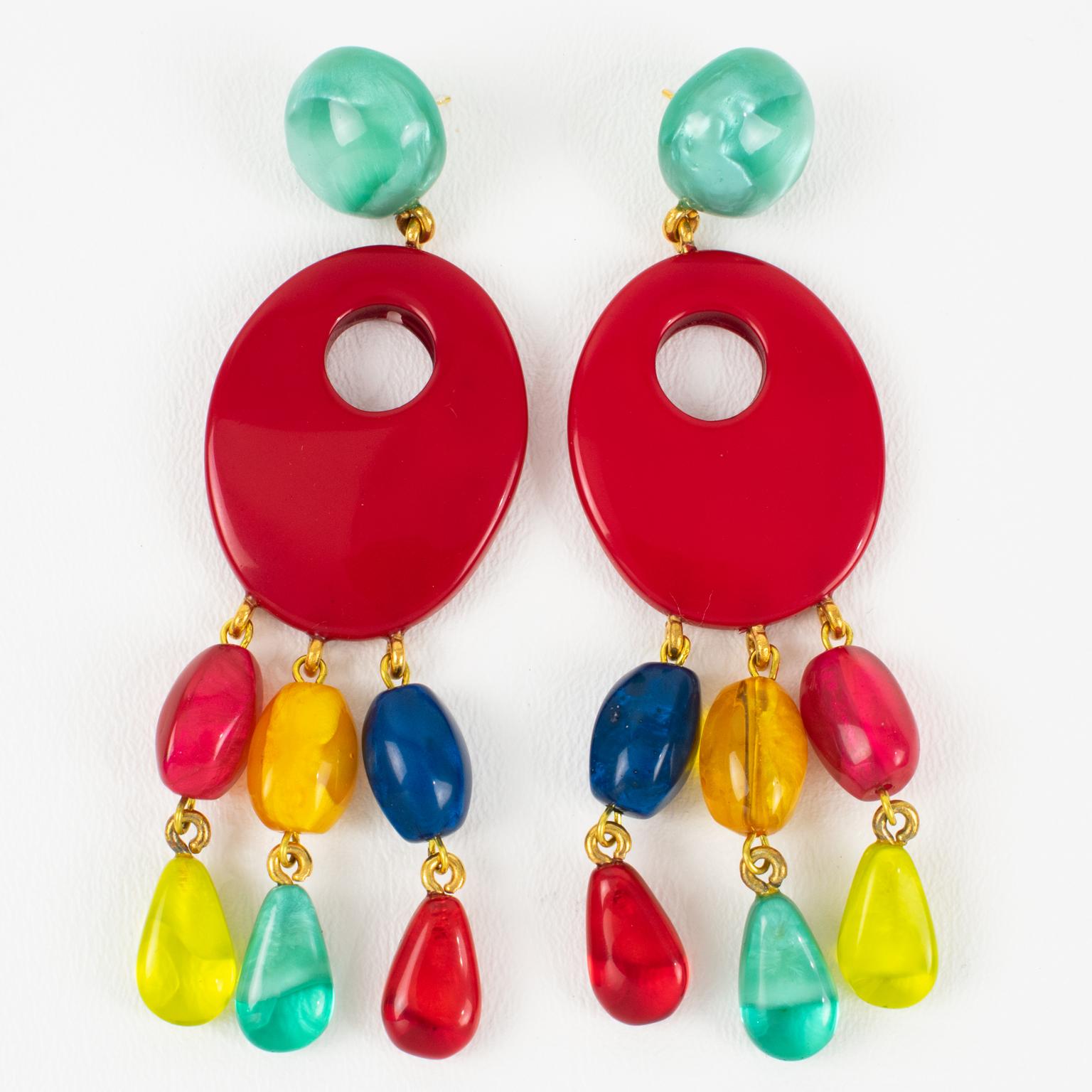 These stunning, oversized pierced earrings by Dominique Denaive Paris feature a sculptural, chandelier-like dangling shape. The carved and see-through oval resin elements are embellished with teardrop charms. The solid bright red color contrasts