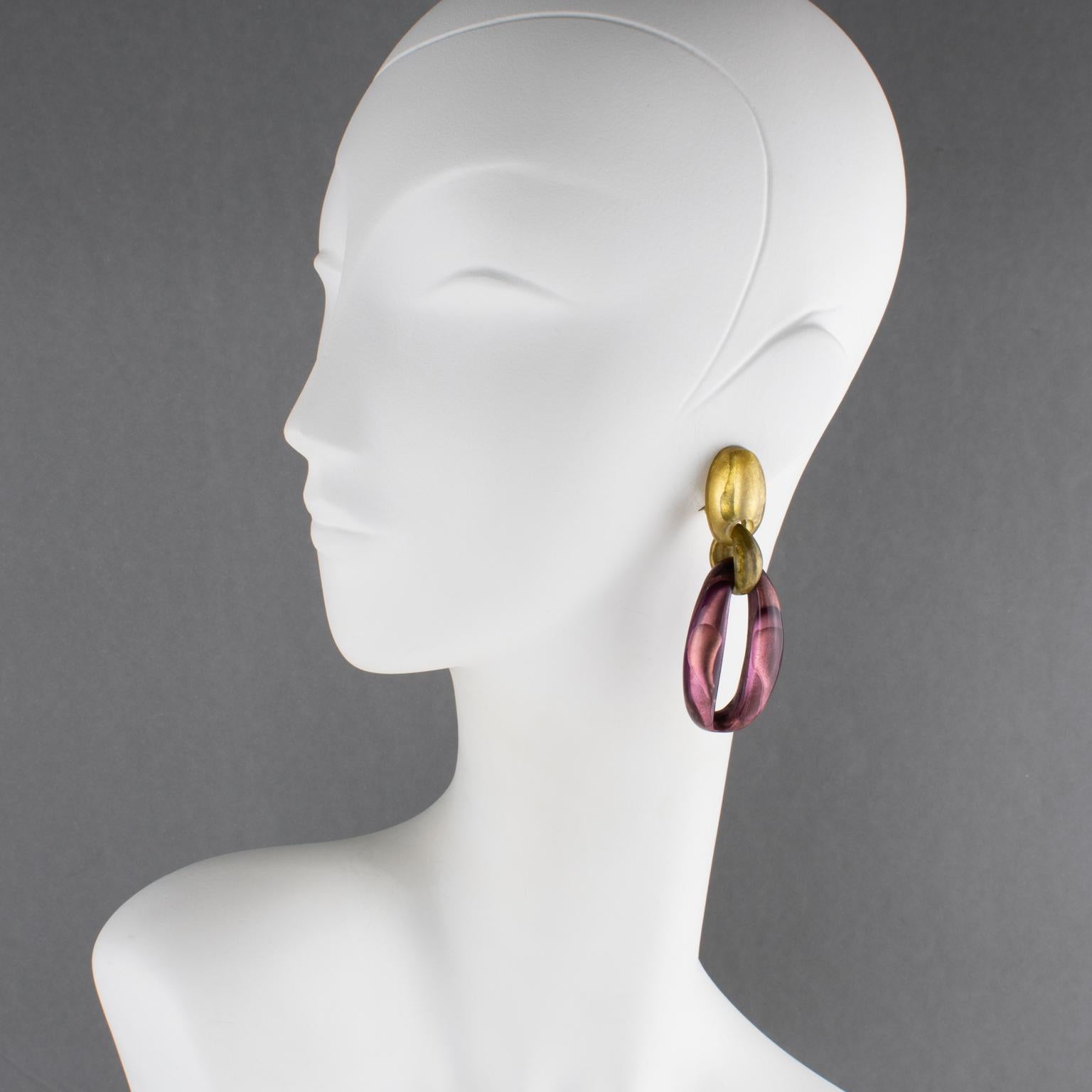 These stunning resin clip-on earrings by Dominique Denaive Paris feature a dangling shape with drops and elongated donuts in a lovely eggplant purple pearlized color contrasted with gold color elements. The engraved signature on the back of each