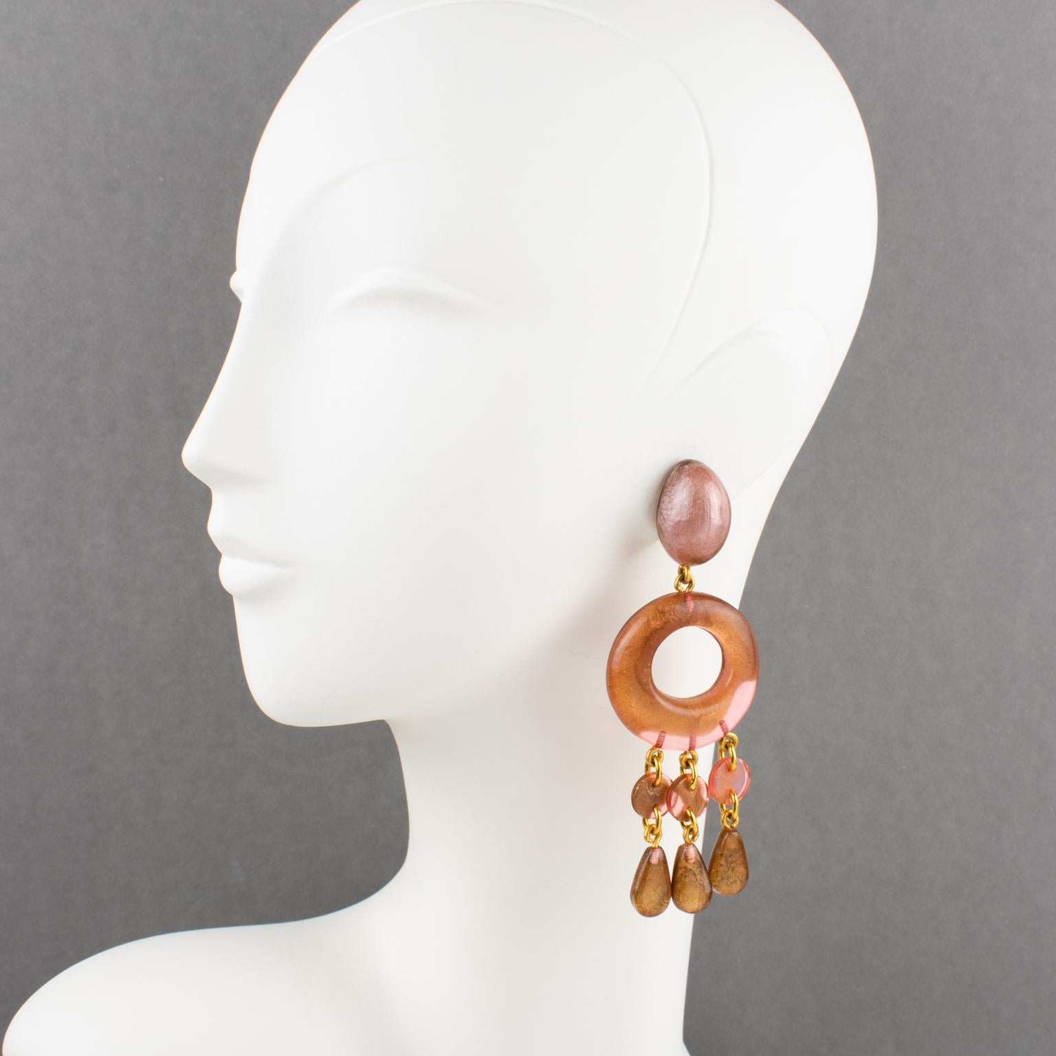 These stunning oversized clip-on earrings by Dominique Denaive Paris boast a sculptural chandelier dangling shape with pearlized carved resin elements and drop charms in a lovely mix of golden brown, rose pink, and lavender-pink colors. The hardware