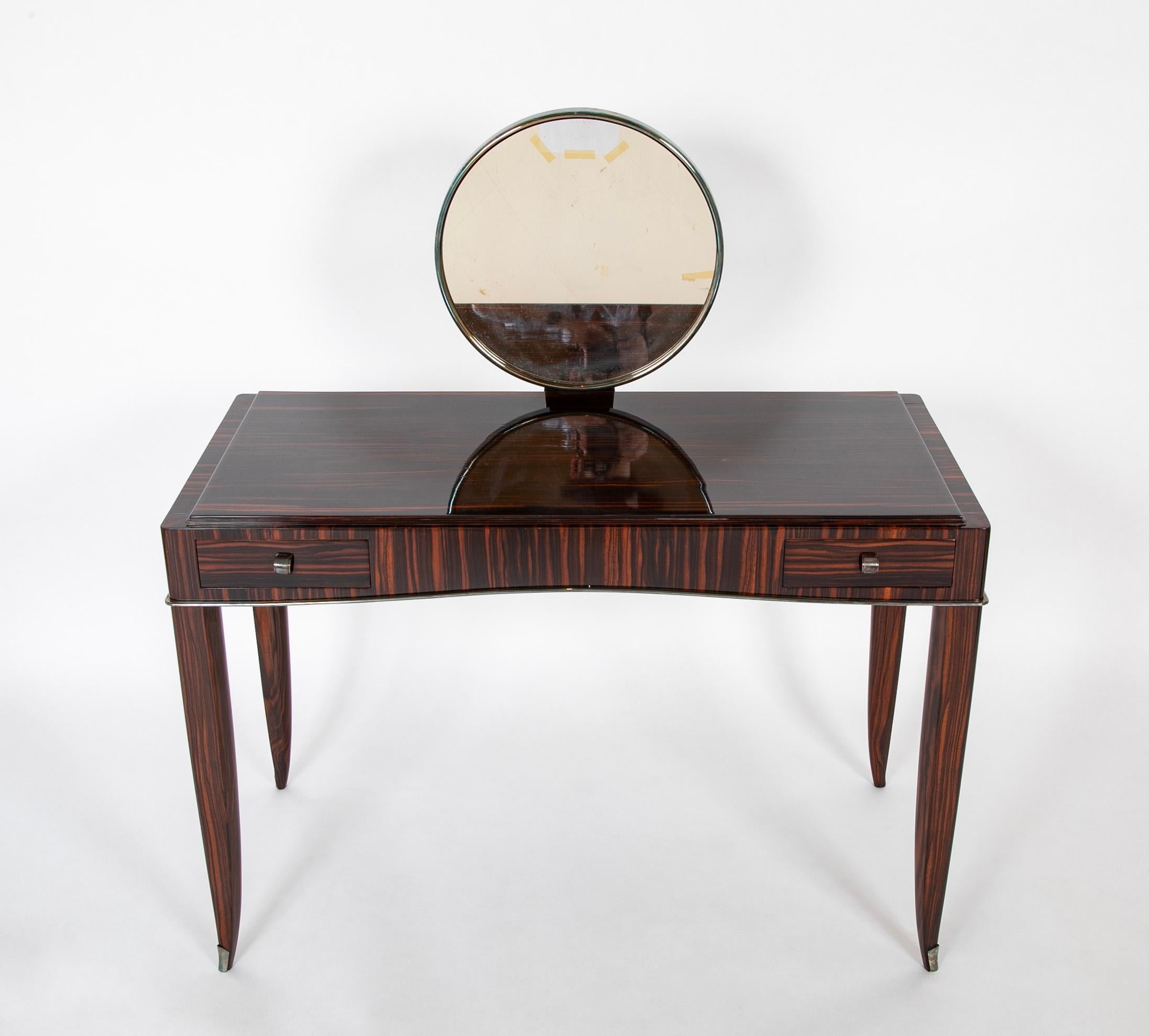 A dressing table / desk designed by  Andre Domin and Marcel Genevriere, better known as Dominique.   The two drawer dressing table is in Macassar Ebony.  The removable silver plated bronze round mirror and hardware (Sabot and trim) were most likely