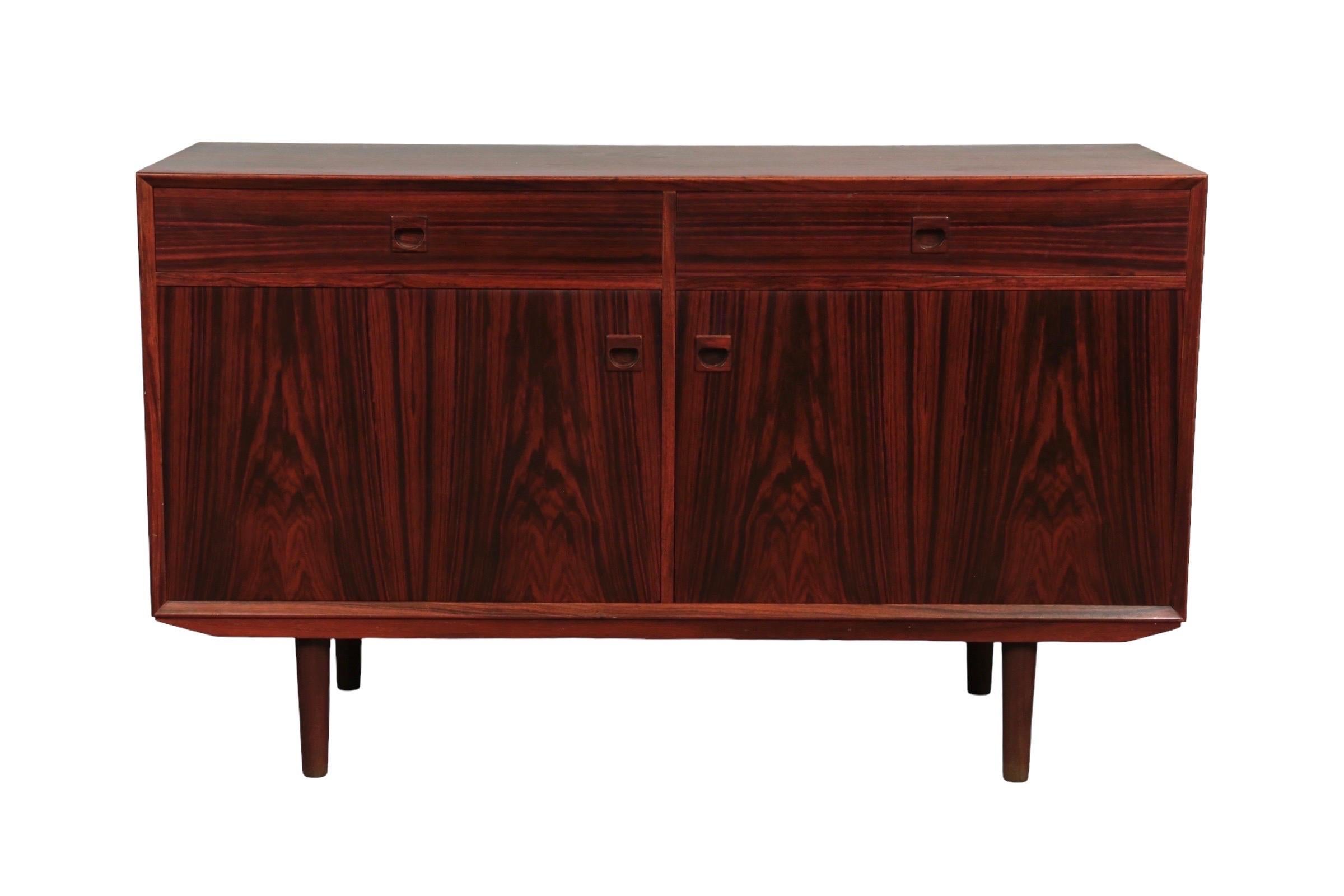 A mid-century credenza by Domino, made of rosewood. Two dovetailed drawers and cabinet doors open with refined recessed handles. Inside is housed a single shelf. Stands on round tapered legs.