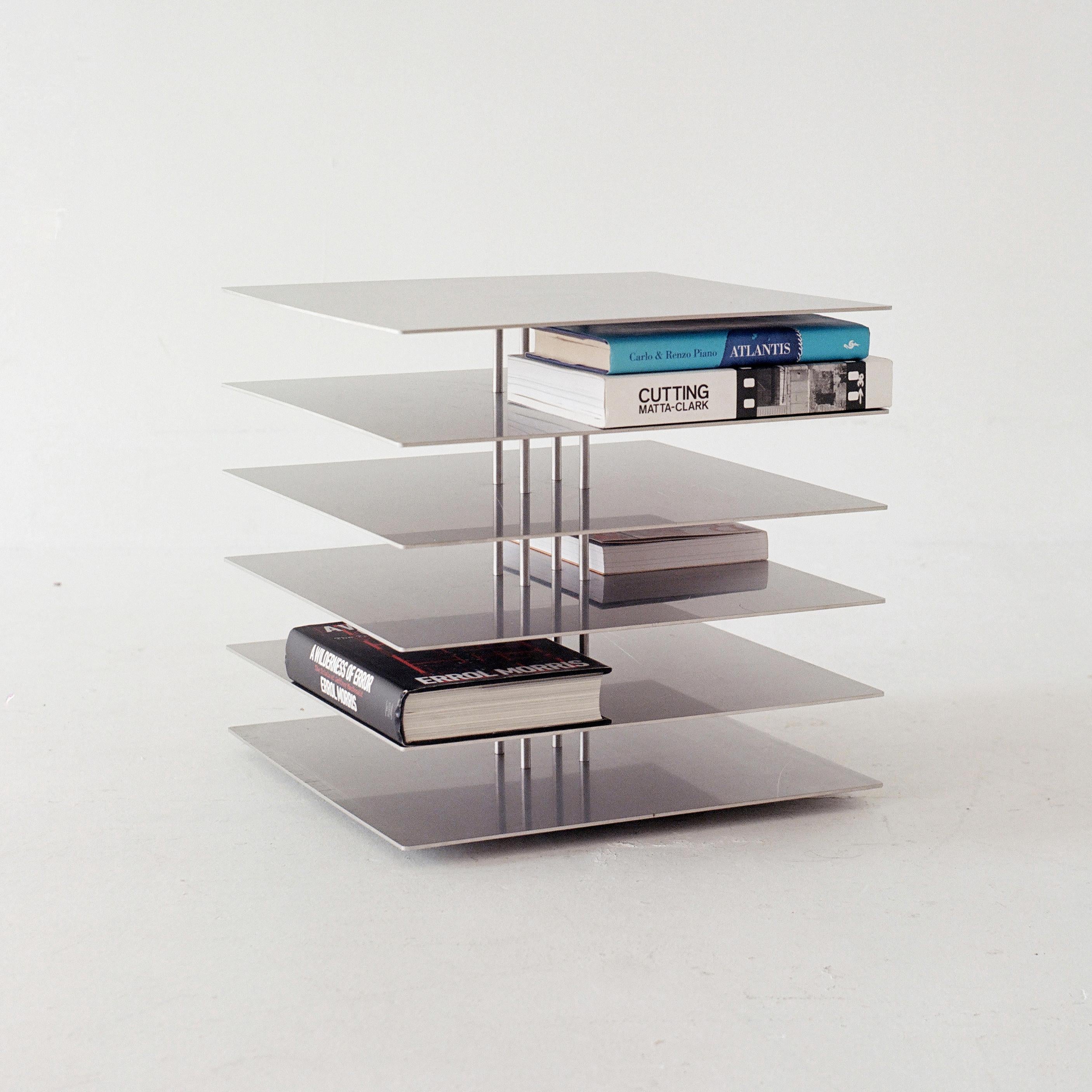 This stainless steel side table is inspired by Le Corbusier’s Dom-Ino House. The minimal form perfectly fits books around the central columns, and at certain angles, the structure disappears, showing only an array of floating metal plates. The piece
