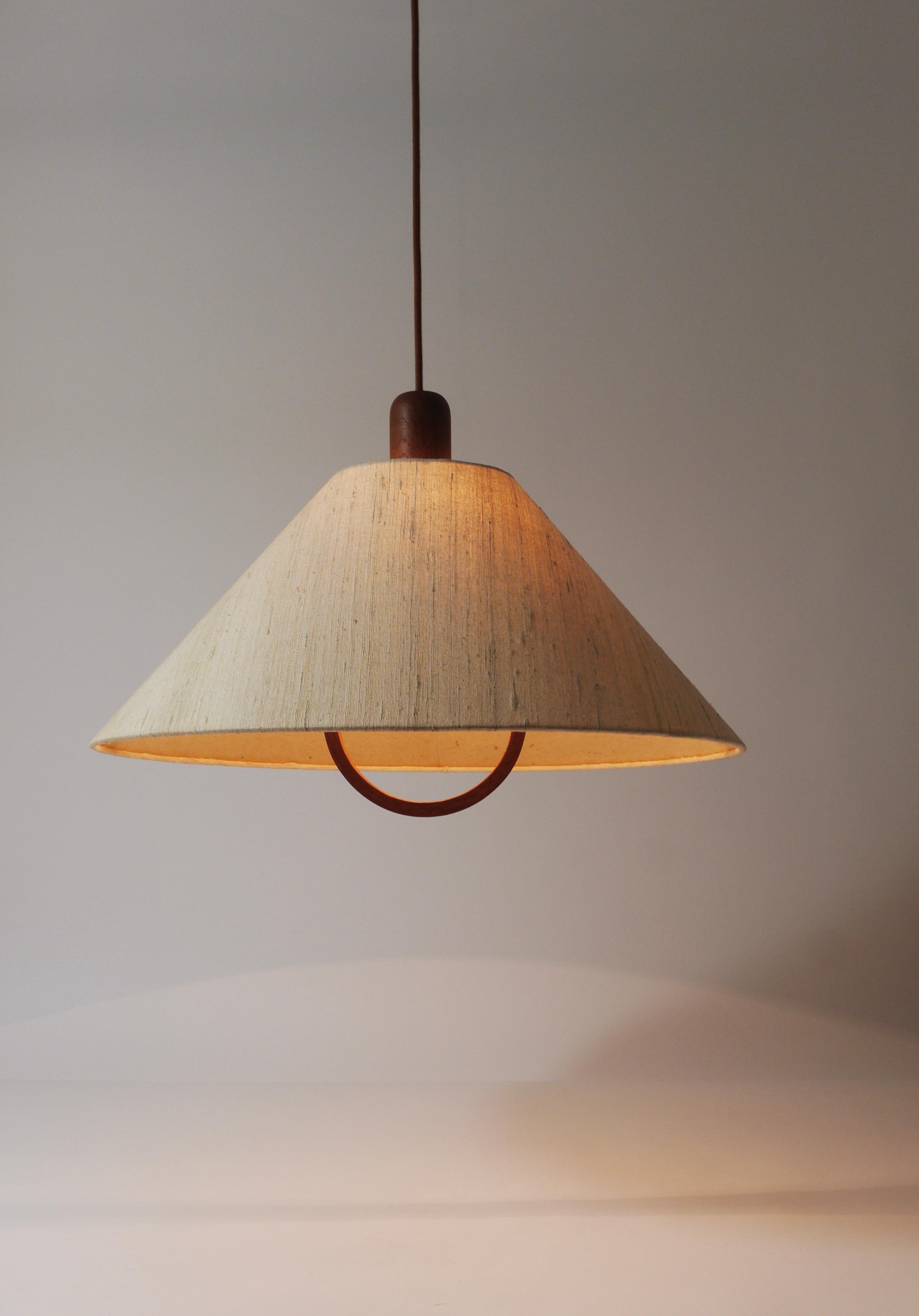 An elegant Danish modern pendant light from the 1970s, crafted by Domus in Denmark. Made of teak, this light features a minimalistic design with a diameter of 22 inches. The lamp retains its original lampshade, which is in good condition and is