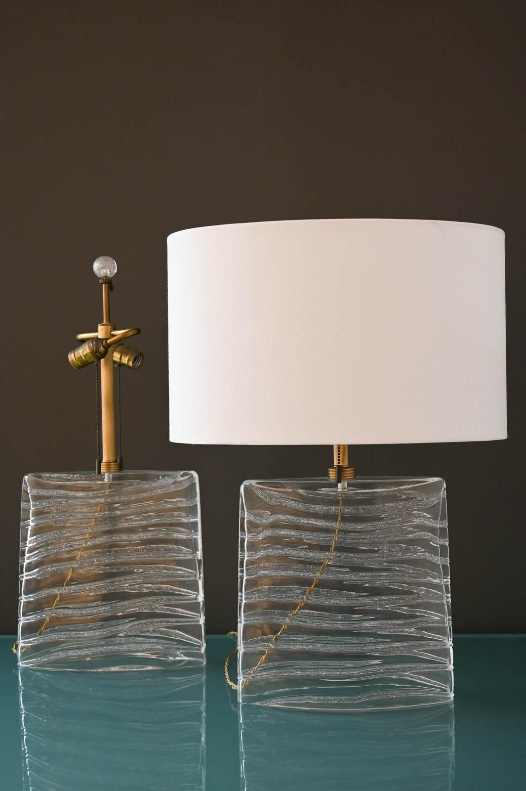 John Hutton for Donghia Murano Glass Lamps in Clear Glass and Brass.  Signed on the base, these beautiful lamps emit soft light and perfect for nightstands or credenza.  Oval shades are NOT included, however we can order new ones for them, please