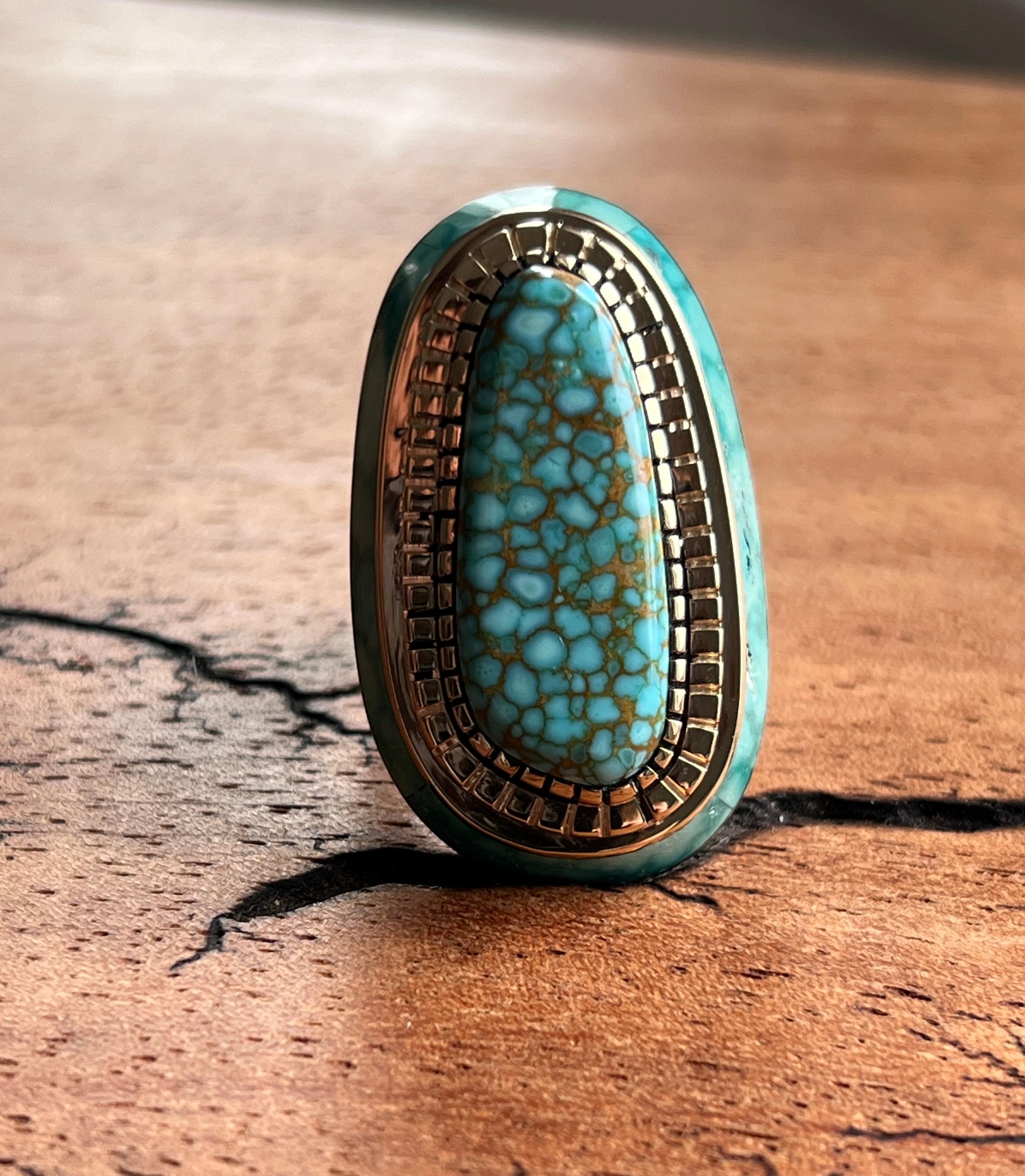 Cette étonnante bague contemporaine illustre l'art de Don Juan du Nouveau-Mexique, avec un magnifique cabochon de turquoise serti dans un chaton en or jaune 14k à la gravure complexe. La turquoise centrale présente de magnifiques motifs matriciels