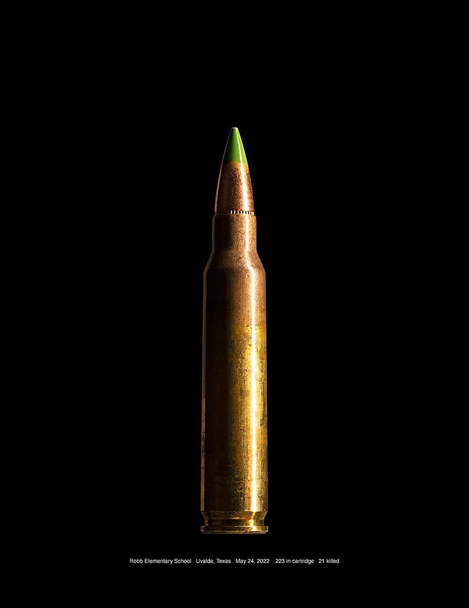 Robb Elementary School, Uvalde, Texas by Don Netzer is a 21.25 x 16.25 inch archival pigment print. The photograph features a bullet with the following text, "Robb Elementary School Uvalde Texas  May 24, 2022   .223 inch cartridge   21 killed" This