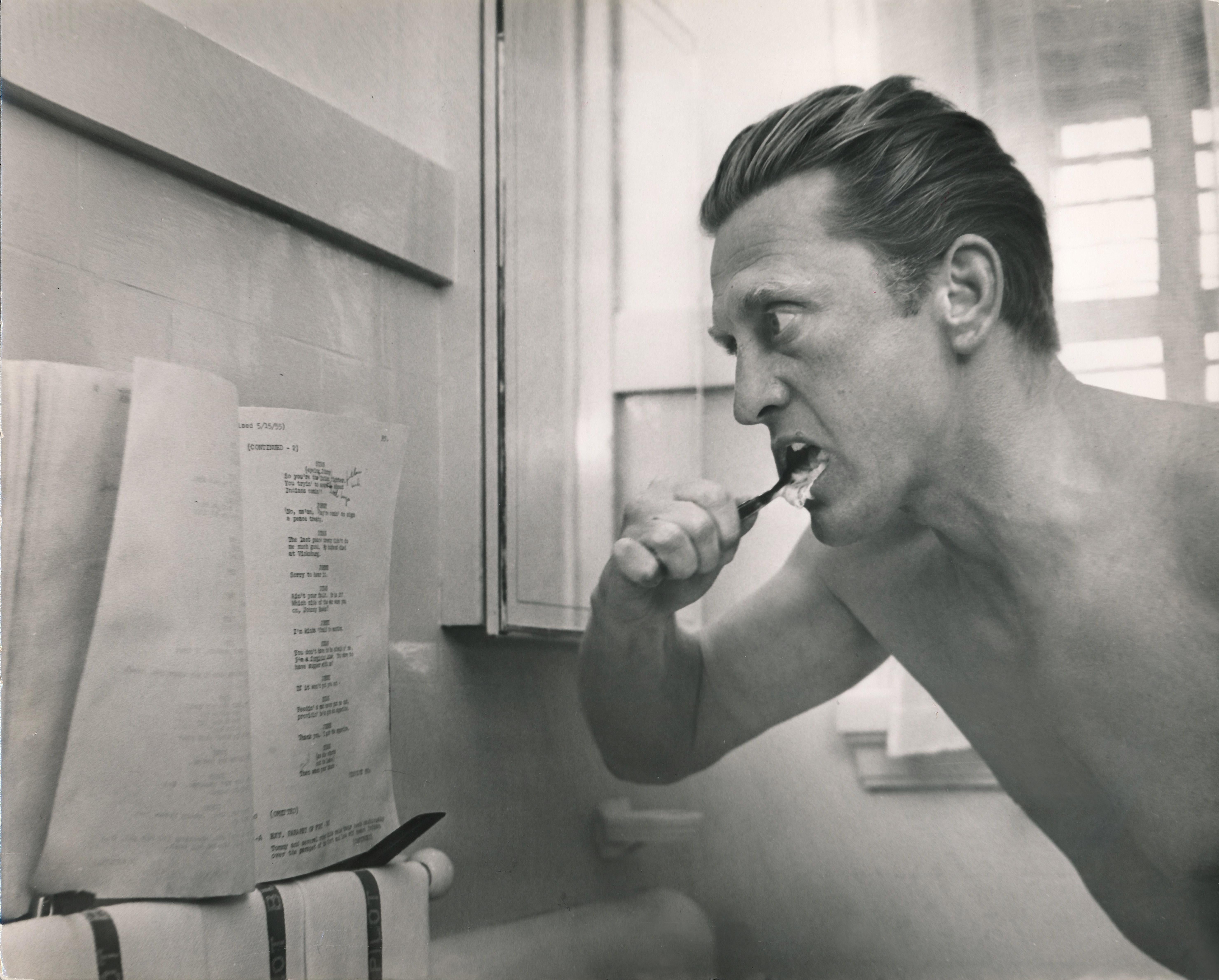 Don Ornitz Black and White Photograph - Kirk Douglas Reading Script While Brushing His Teeth Fine Art Print