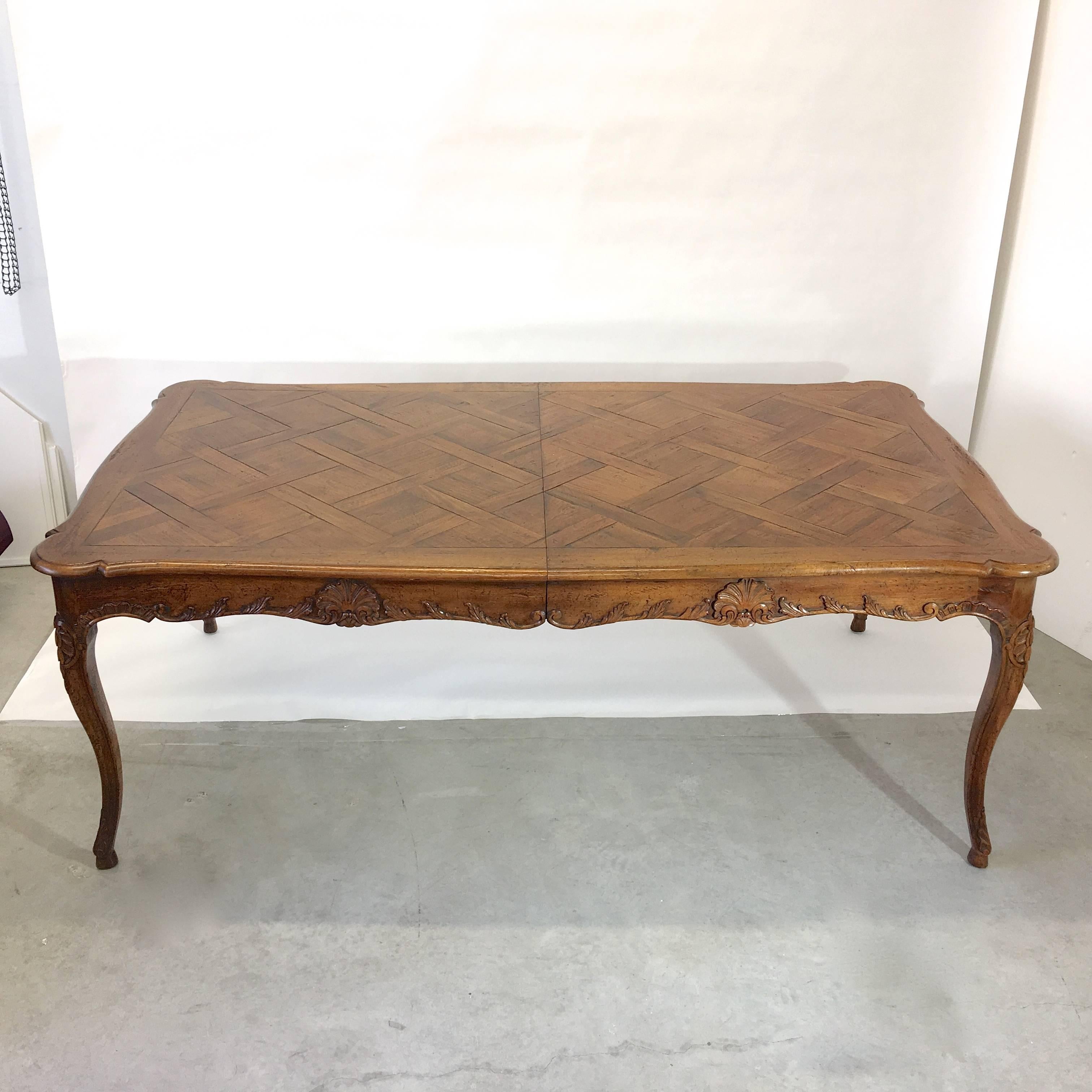 Majestic 14.4 feet long dining table by legendary carvers Don Ruseau of East 53rd Street New York City. 
Bench made French Provincial walnut with parquetry top, hand carved cabriole legs and scalloped apron with shell motif. Four 24 inch leaves with