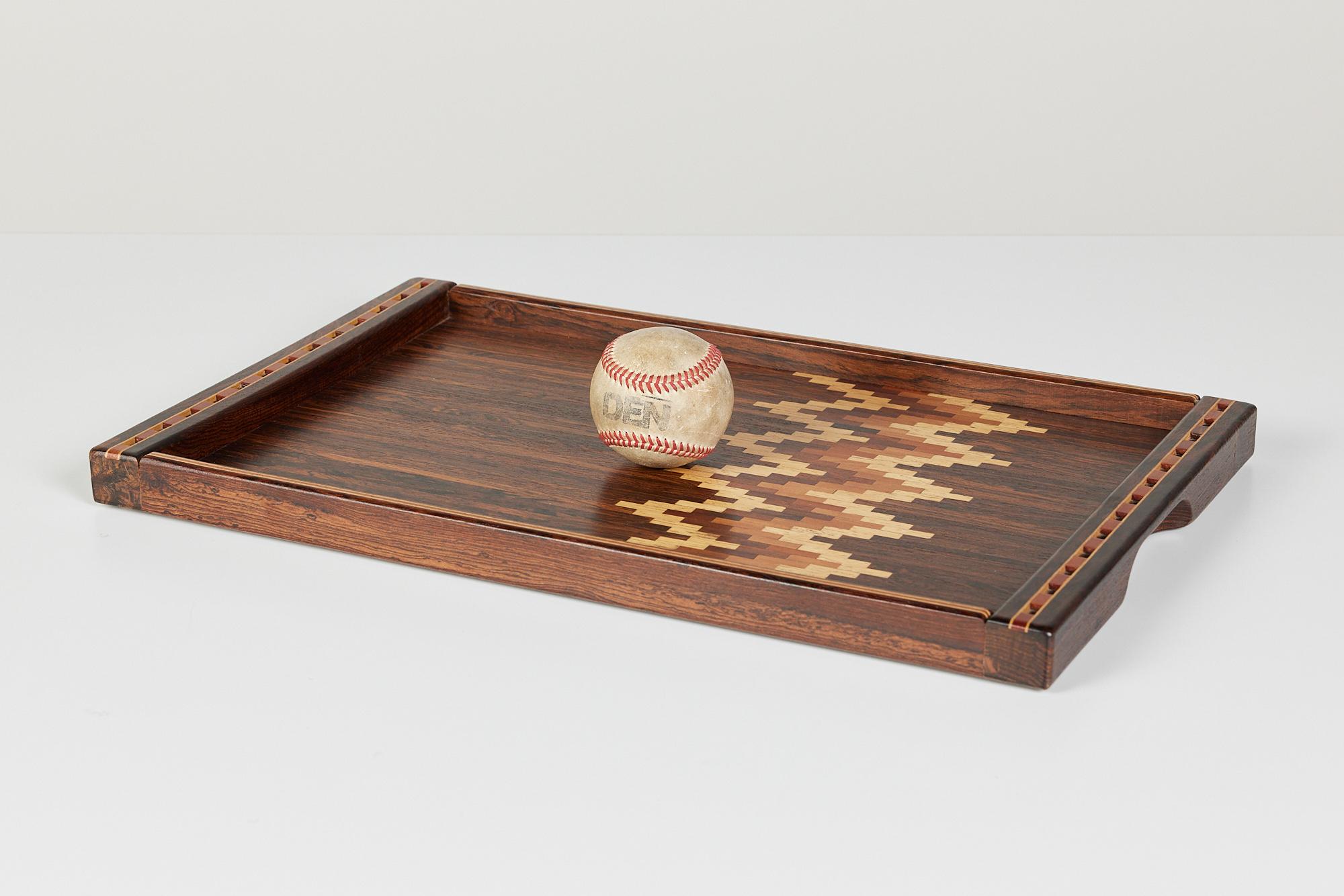 A rosewood serving tray with integrated handles by Don Shoemaker for his company Señal in the 1960s. The surface of the tray has a pixelated chevron-patterned parquet detail in exotic woods.

Label on bottom reads, “Designed by Don S. Shoemaker,