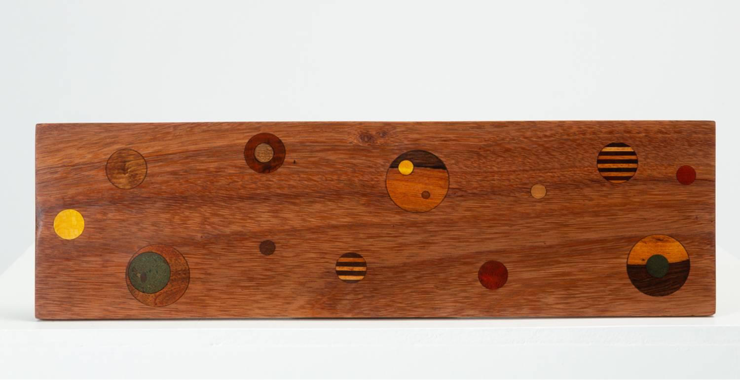 A rosewood cutting or serving board designed by Don Shoemaker for his company, Señal, in the 1960s. Known as the G-27 “Planetarium Board,” the surface of the piece is inlaid with exotic woods and stone in intersecting and concentric geometric forms.