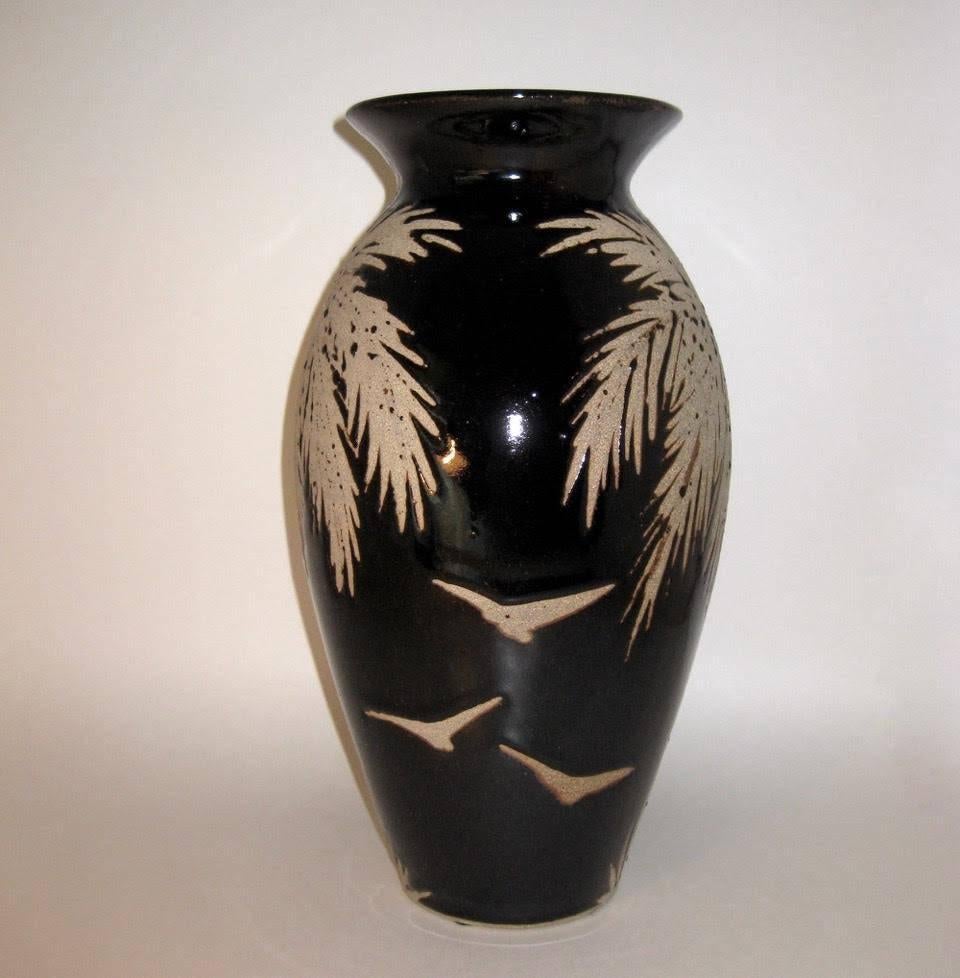 Studio art stoneware pottery, tall tropical vase with a palm tree and sea bird design. The vase is glazed in a deep, rich dark brown, gloss glaze, with an unglazed, reverse design featuring two palm trees and six seabirds. The piece is by listed