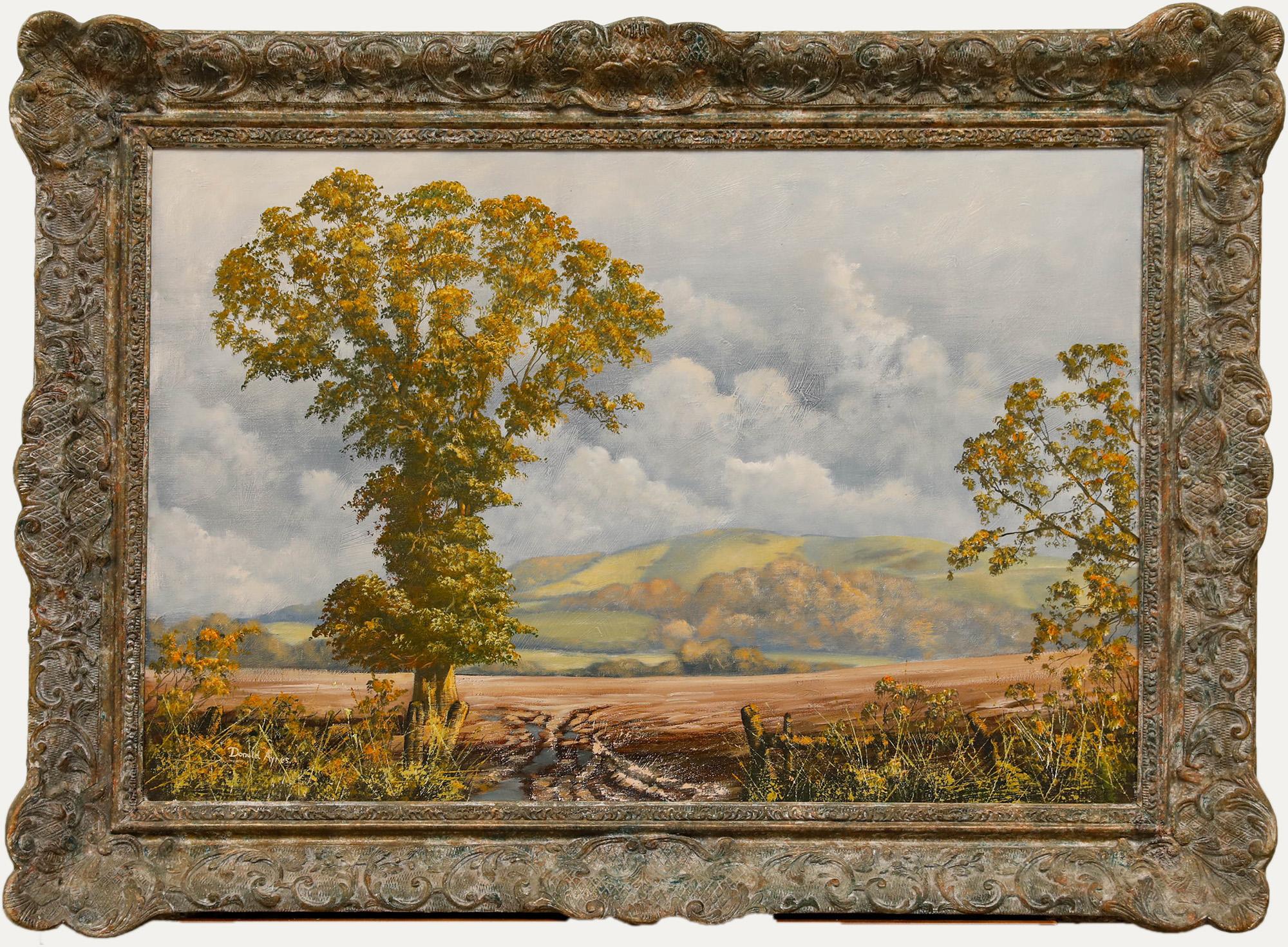 Este sereno cuadro de paisaje capta una bucólica escena campestre, con un majestuoso árbol de hojas doradas dominando el primer plano sobre un fondo de colinas ondulantes y un cielo nublado. El marco ornamentado y desgastado añade un toque clásico a