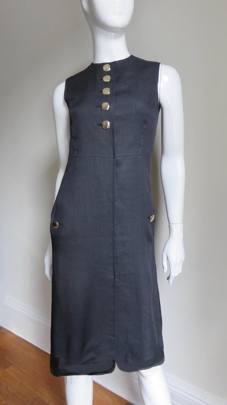 A gorgeous black linen shift dress by the great American designer Donald Brooks.  It is sleeveless with a crew neckline, 5 gold metal buttons and bound buttonholes at the front chest  and hip seam pockets with matching gold buttons.  The skirt