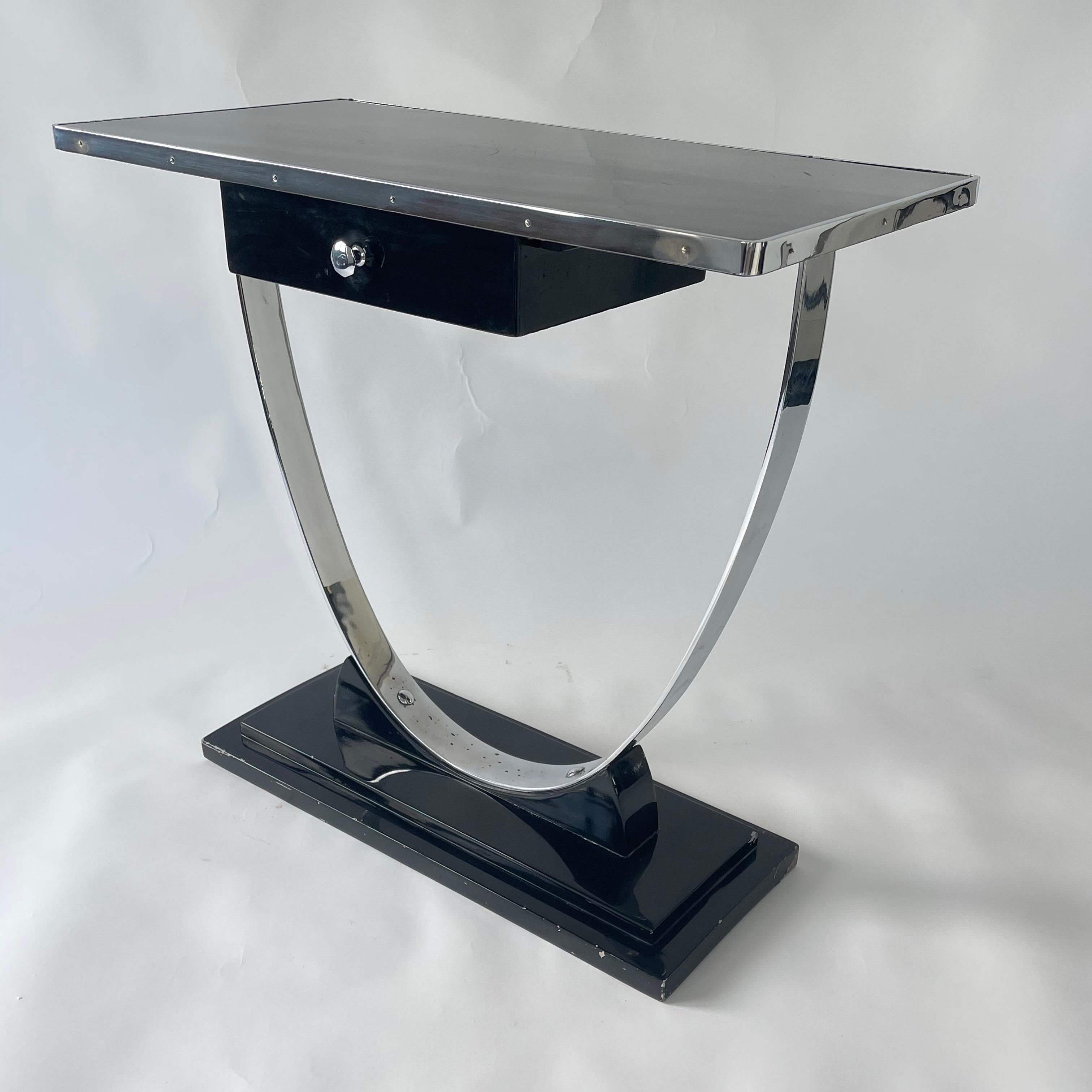 Machin age stromlinienförmiger Art Deco Konsolentisch mit schwarz lackiertem Holzsockel und einer Platte, die von einer verchromten Stahlparabel mit einer Schublade und einem verchromten Griff getragen wird.  Donald Deskey zugeschrieben, USA, 1930er