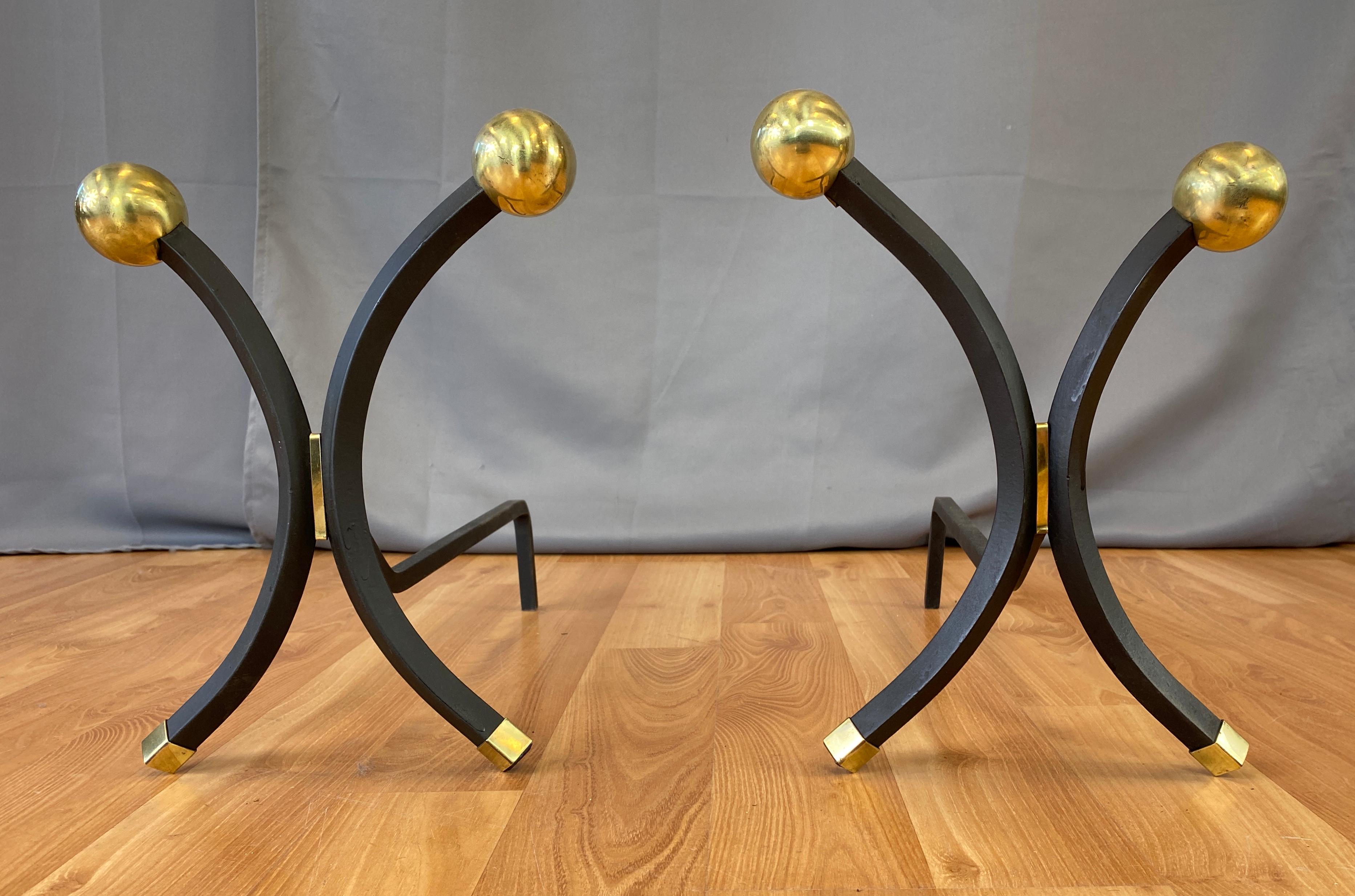 A striking pair brass and iron andirons by important Art Deco and early midcentury designer Donald Deskey. 

Polished brass balls atop of a pair of curved wrought iron fronts which end at square brass feet, behind is the long wrought iron third