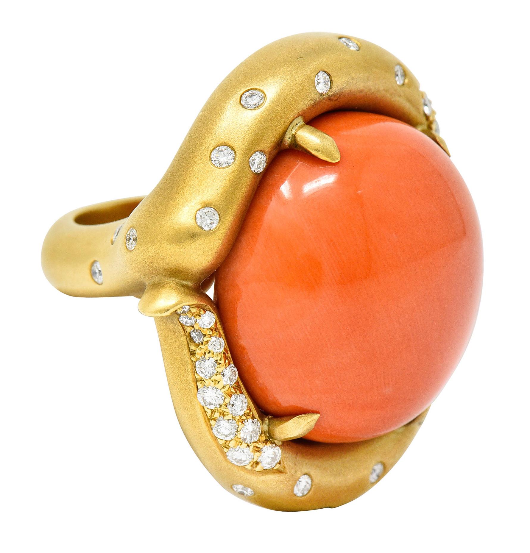 Bypass style ring centers a large round coral cabochon measuring approximately 22.8 mm

Opaque with very uniform pastel pinkish orange color

With a matte gold tendril surround accented by round brilliant cut diamonds

Weighing in total
