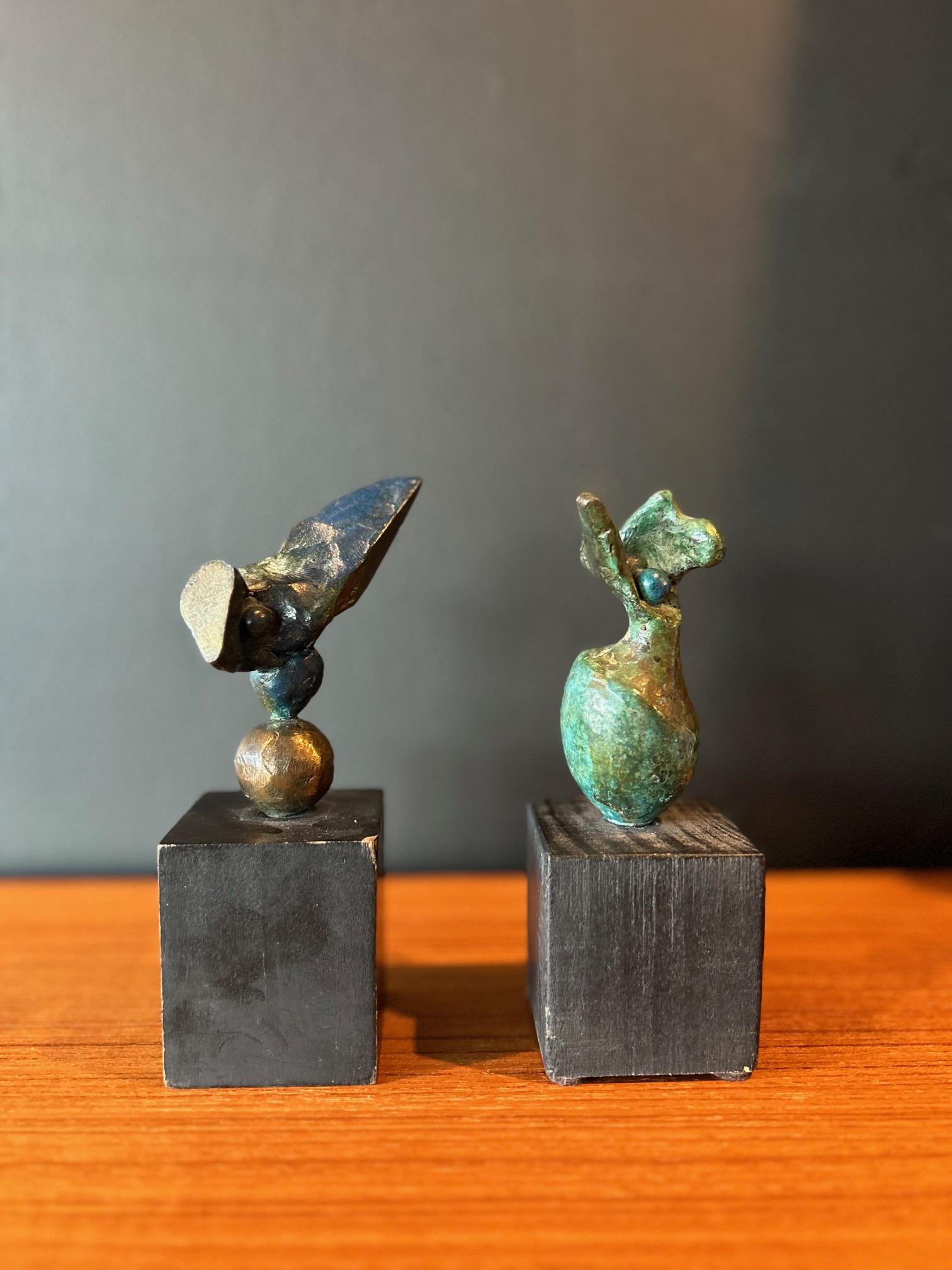 Set of two small abstract bronze sculptures in deep teal/turquoise tones by artist Donald Locke set on black square wood bases. One of the organic forms is punctuated by shapes featuring a polished metallic splice and the other teal figure bears two