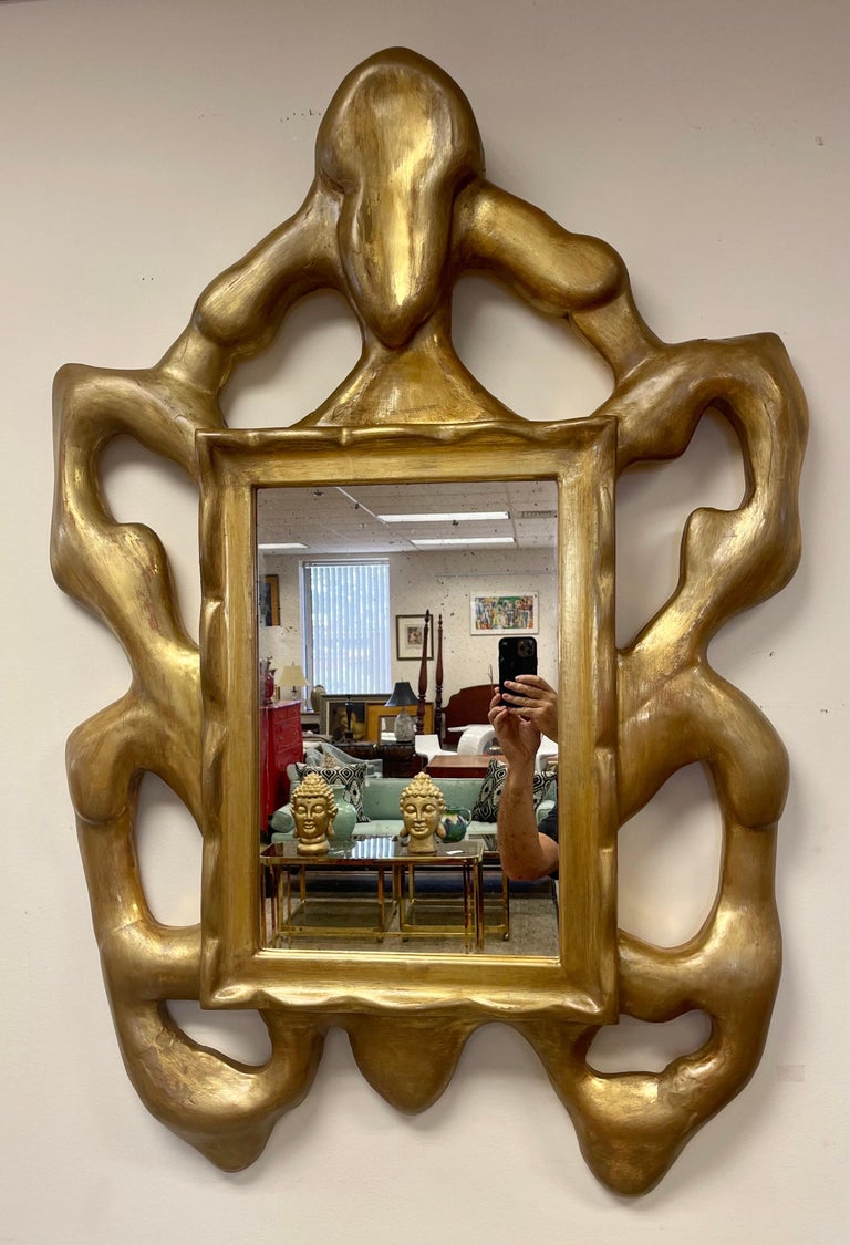 A Donghia hand carved wood frame with freeform, organic lines. With a gold finish on the frame and antiqued patina on the mirror itself, this luxe piece hints at traditional styles but feels fresh and modern. Color is gold ton and ther si some age