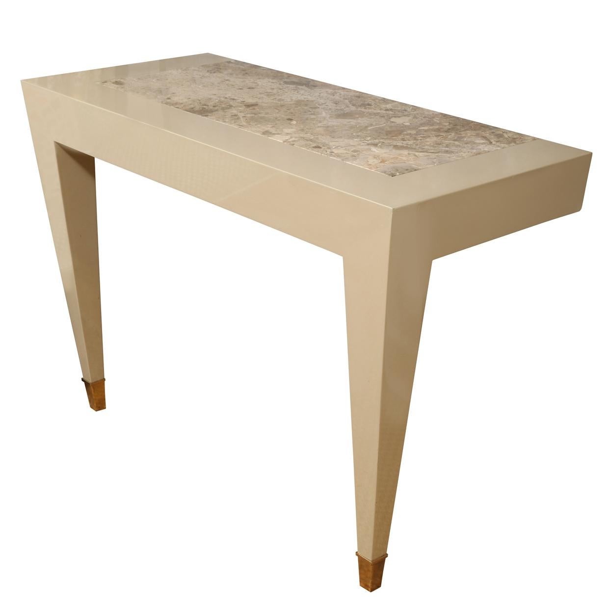 A Mid-Century tan lacquered wall console from Donghia with stone inlay top, angular tapered legs with metal caps at the feet. This chic table is priced as a single console table.  Two tables are available and would look fabulous flanking a