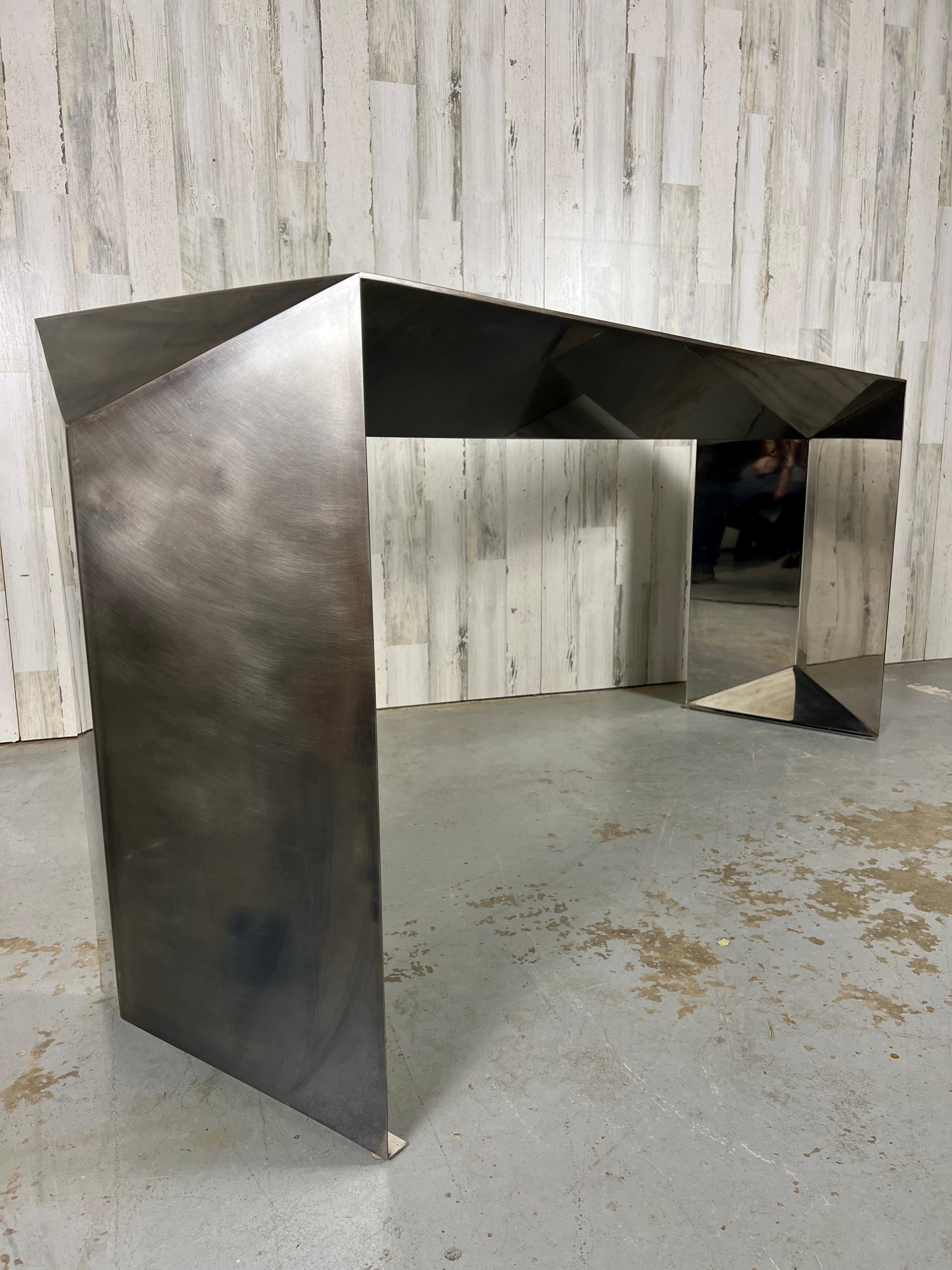 Metal console table in a hand rubbed patina finish on exterior and a mirror polished finish on interior. Inspired by folding paper and realized in sheet metal, this table's shape has a bold geometric design that is distinct in any application.
 