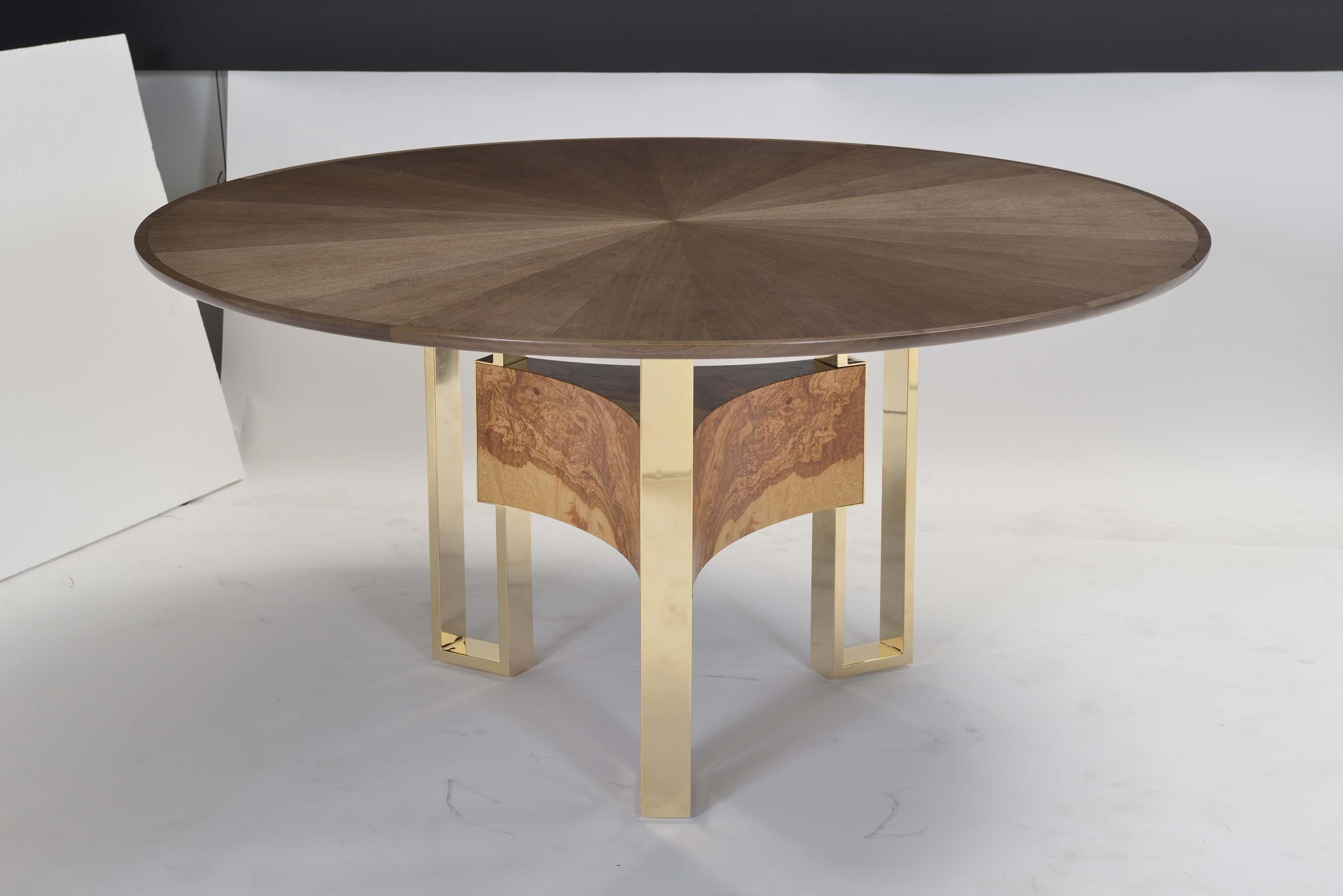 Round dining table veneered in quartered walnut, bookmatched in a starburst pattern with quarter sawn walnut solid bands in an open grain finish in a medium sheen. Choose between polished gold-plated or satin smoke metal legs joined together with a