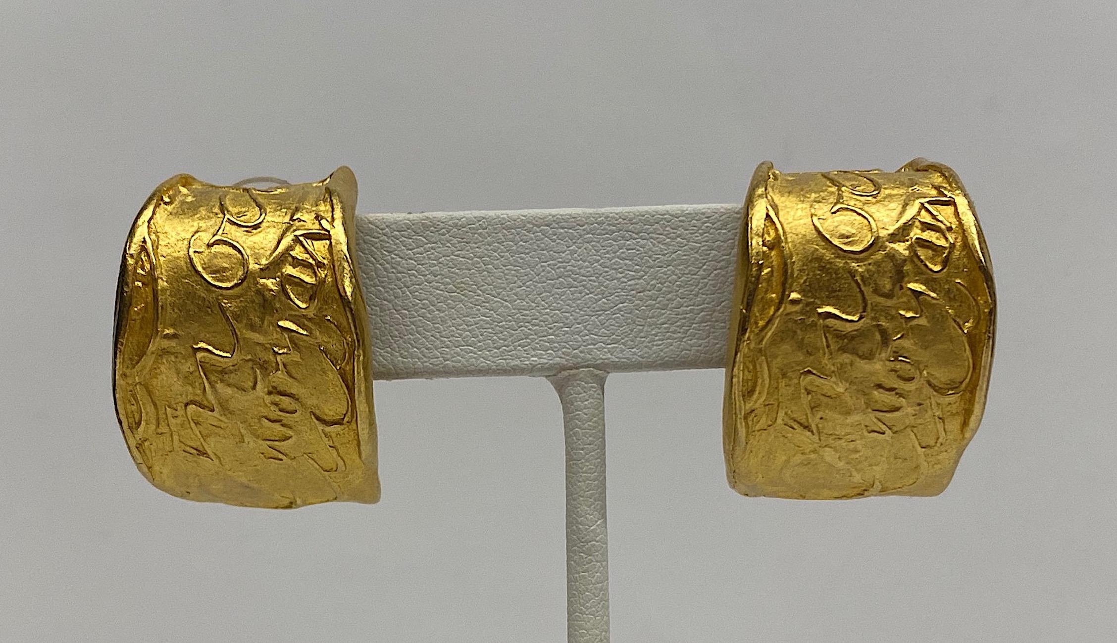 A wonderful pair of satin gold plate Donna Karen wide hoop earrings from the 1980s. Each earring has a textured surface and sculptural quality. The abstract surface design includes the script words 