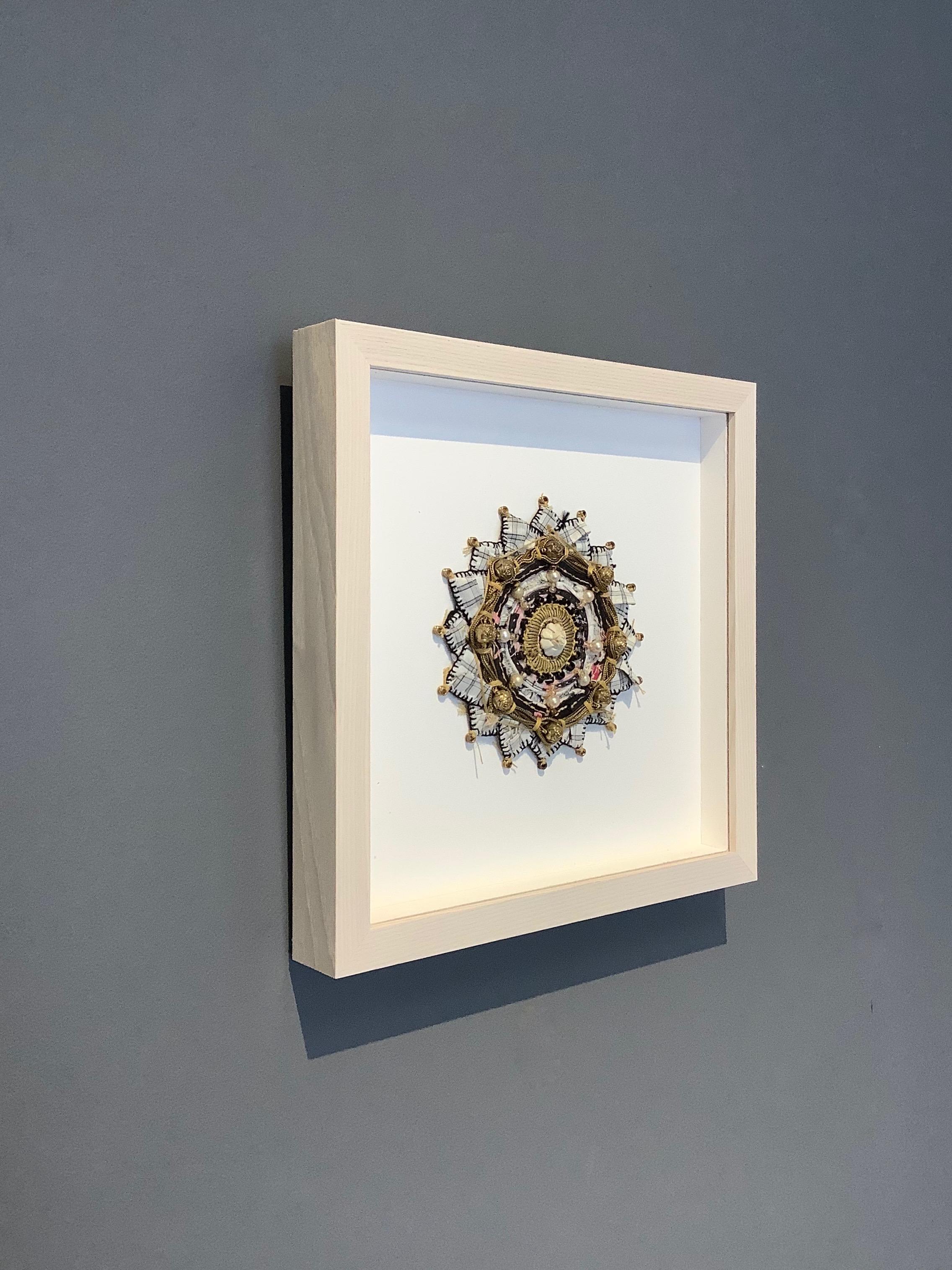 Mixed media mandala by Donna Sharrett containing guitar string ball-ends, clothing, needlework, jewelry, and thread. A carved ivory rose bead at the center is outlined with gold threading and a circle of pearls, is surrounded by carved gold rose