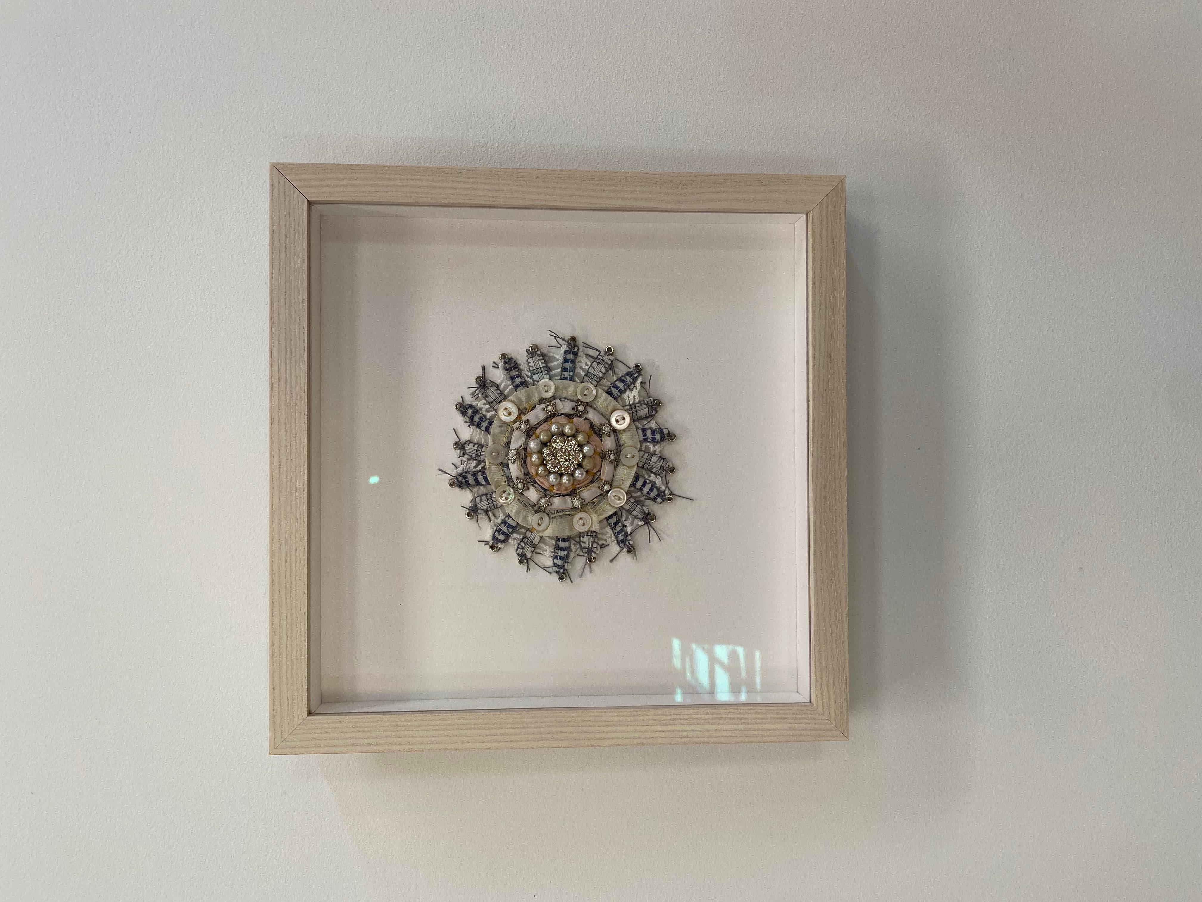 This mixed media mandala by Donna Sharrett contains guitar string ball-ends, clothing, needlework, jewelry, and thread. Glittering gold faceted beads at the center are outlined with a circle of pearls in ivory and gold surrounded by pale peach