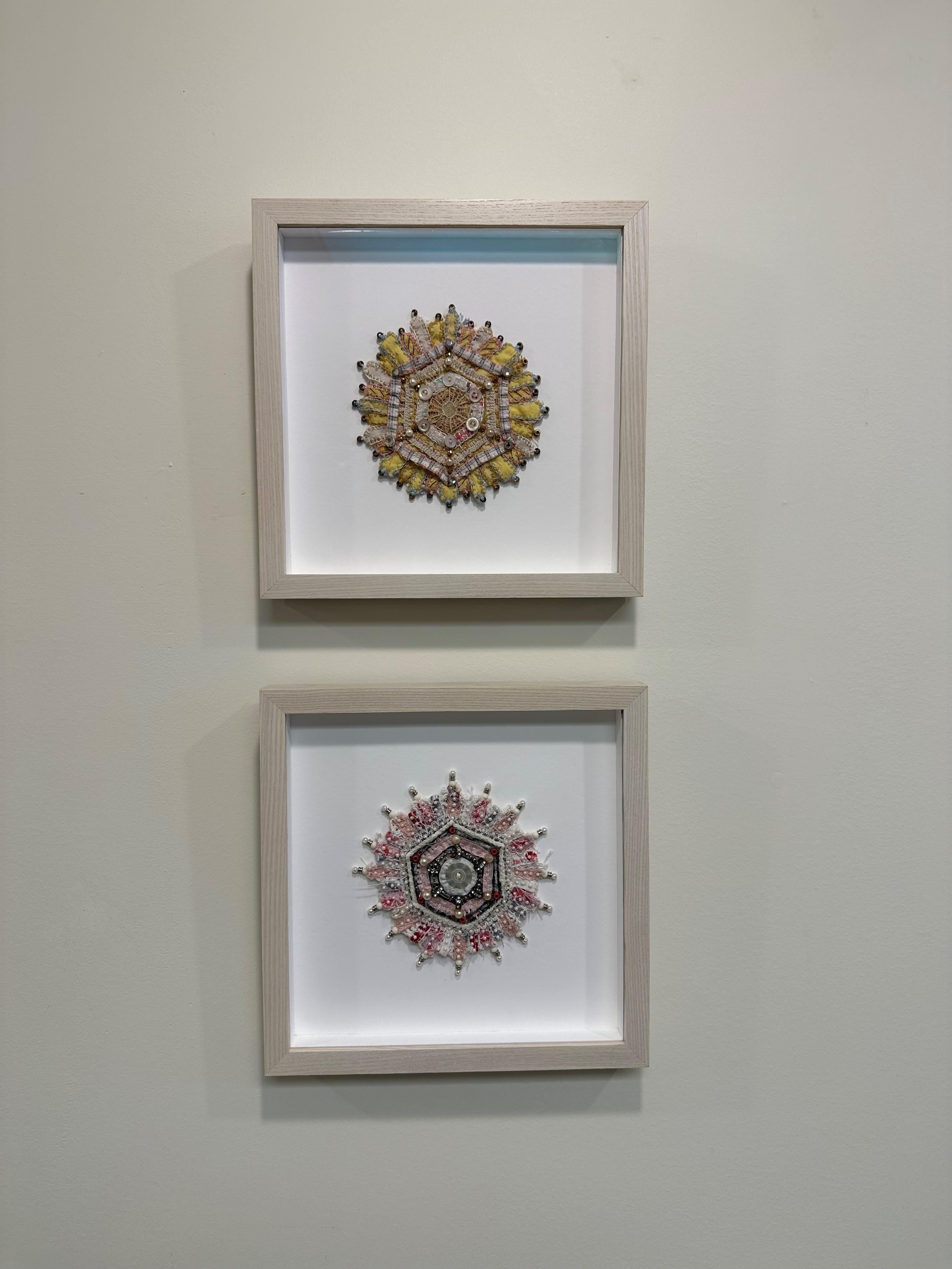 This mixed media mandala by Donna Sharrett contains guitar string ball-ends, clothing, needlework, jewelry, and thread, and is framed in a square 10 x 10 inch light natural wood float frame (5 x 5 inches unframed). 

Rhinestone studded beads and a