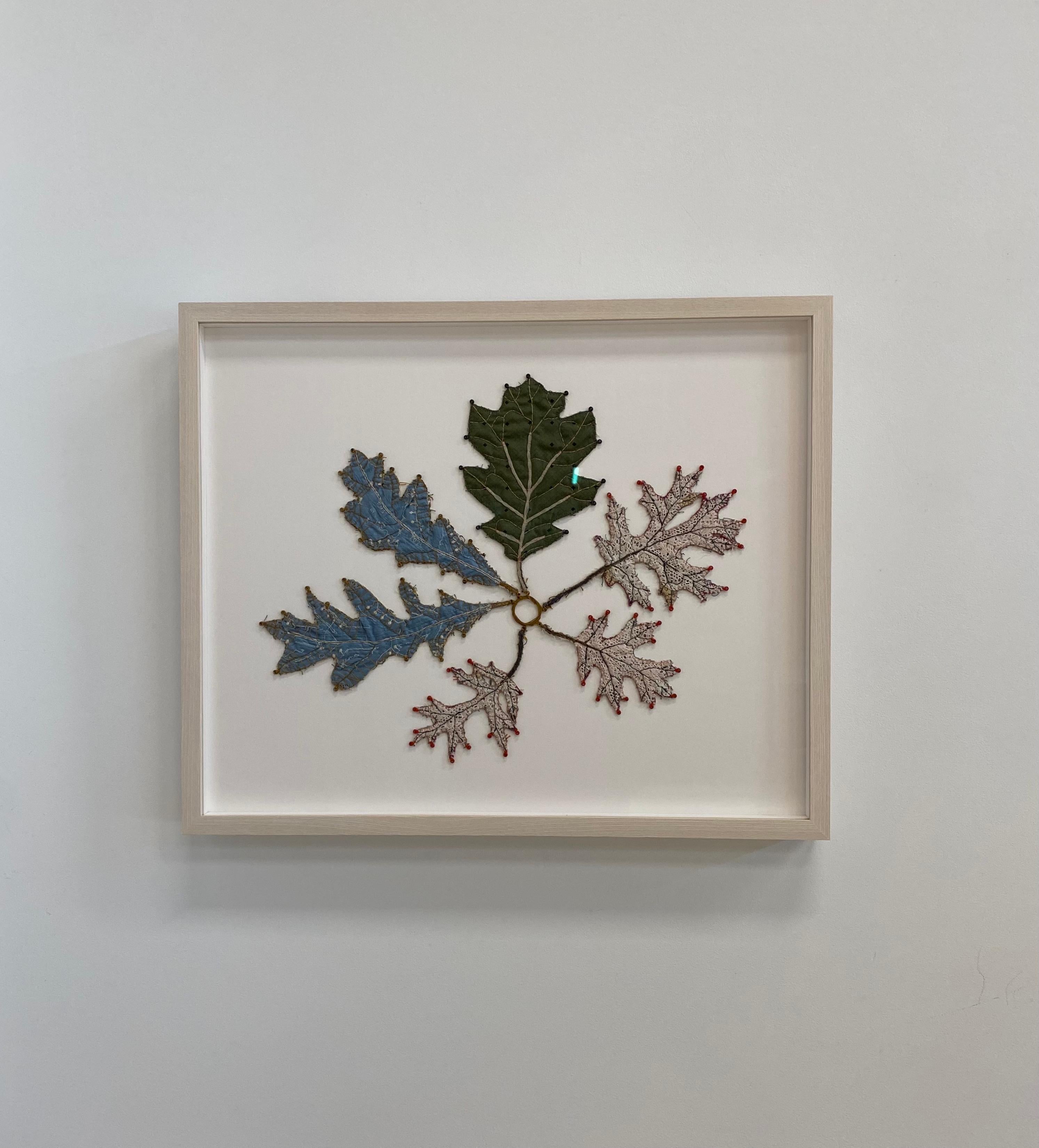 This contemporary mixed media botanical artwork by Donna Sharrett is comprised of fabric, trimming, thread, guitar strings and ball-ends, and framed in museum glass with all archival materials in a light natural wood float frame. Leaves made of a