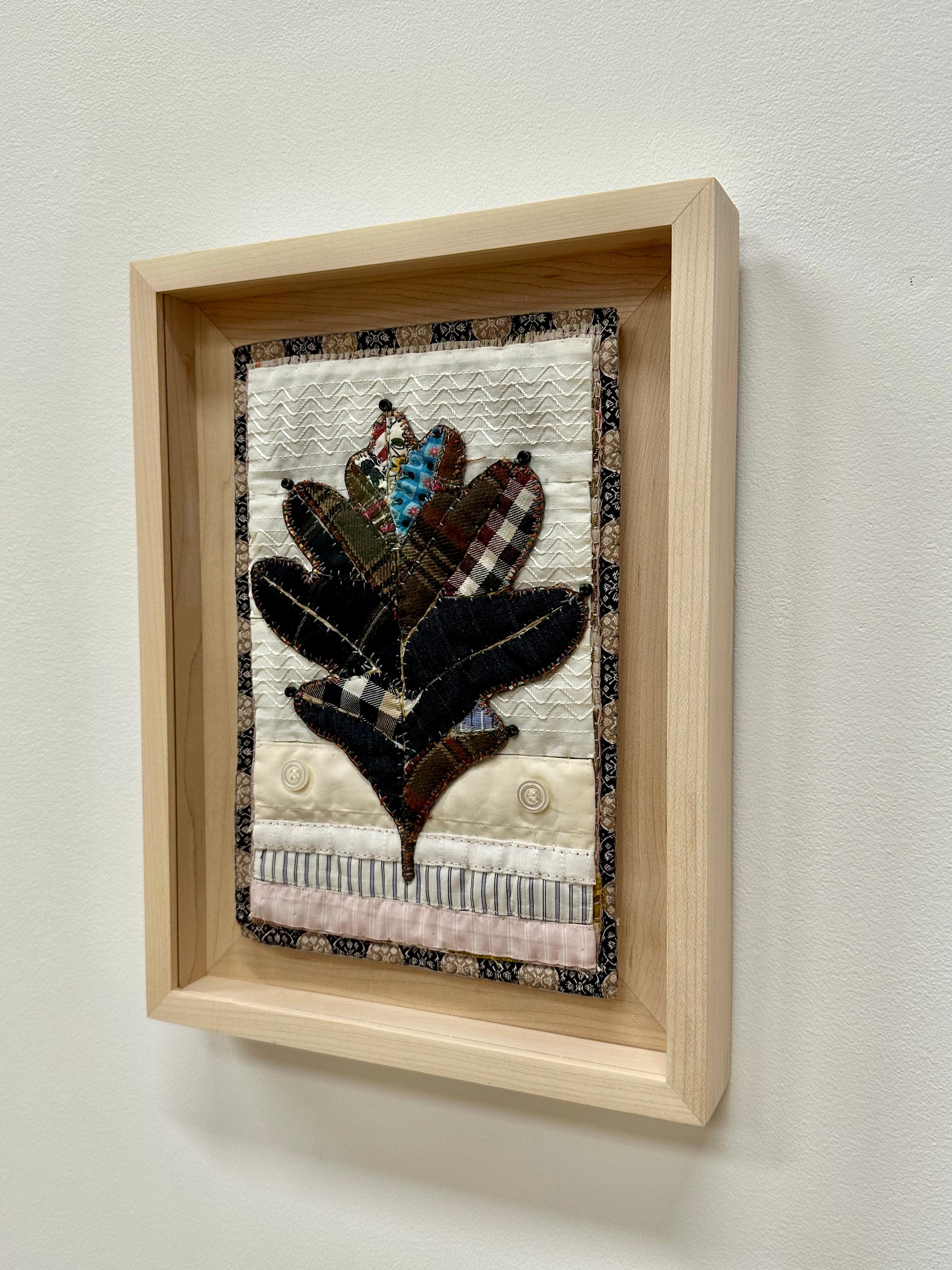 In questa opera d'arte tessile botanica contemporanea, una foglia di quercia bianca è composta da indumenti donati delicatamente cuciti, tessuti, nozioni e corde di chitarra, in marrone scuro, blu scuro, un motivo a scacchi e un motivo botanico tra