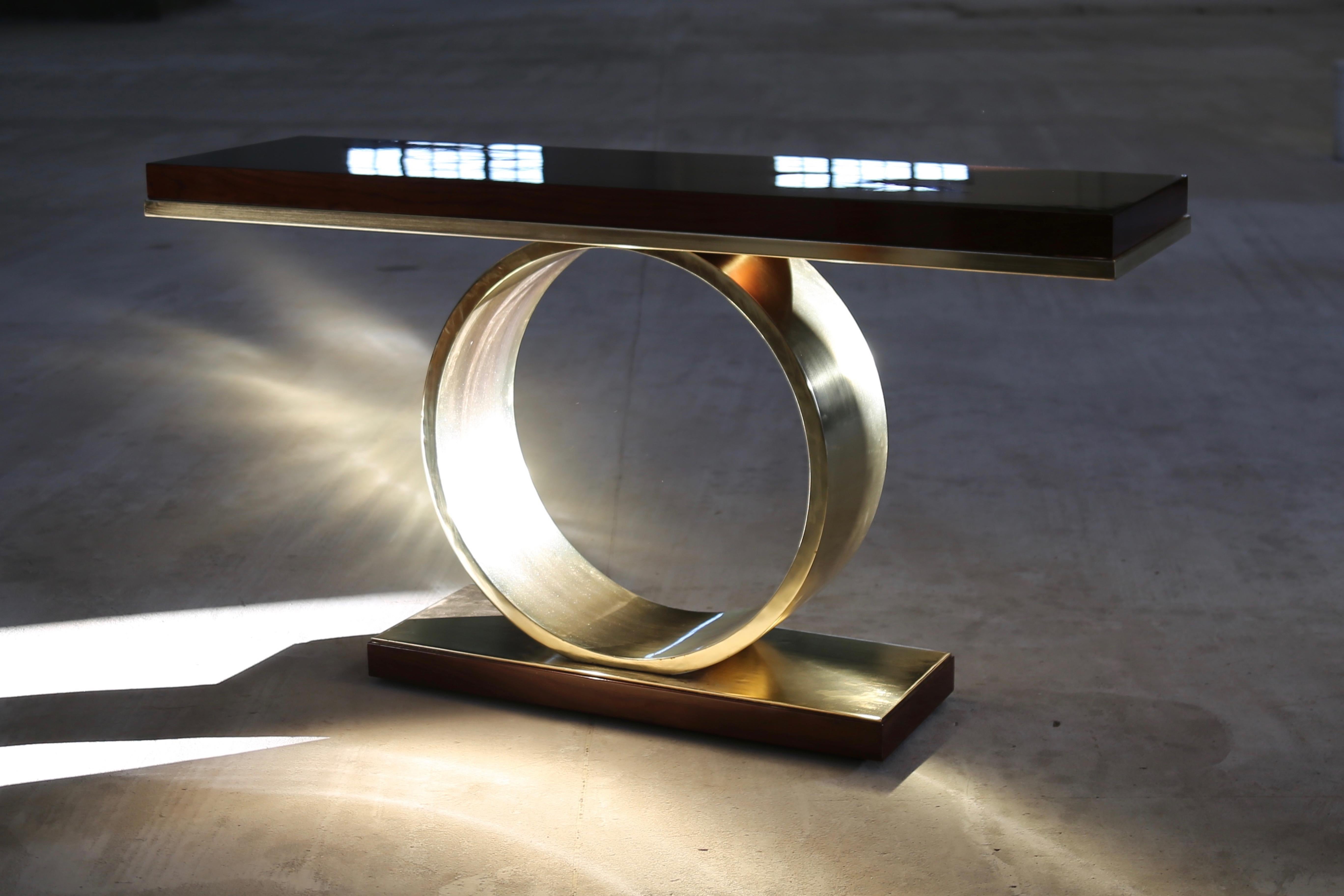 Donte Polished Bronze and Wood Sculptural Console Table.

The Donte console table features a ring-shaped metal base, shown here in polished Bronze, supporting a high gloss wood top. Available in any species, size, or finish.