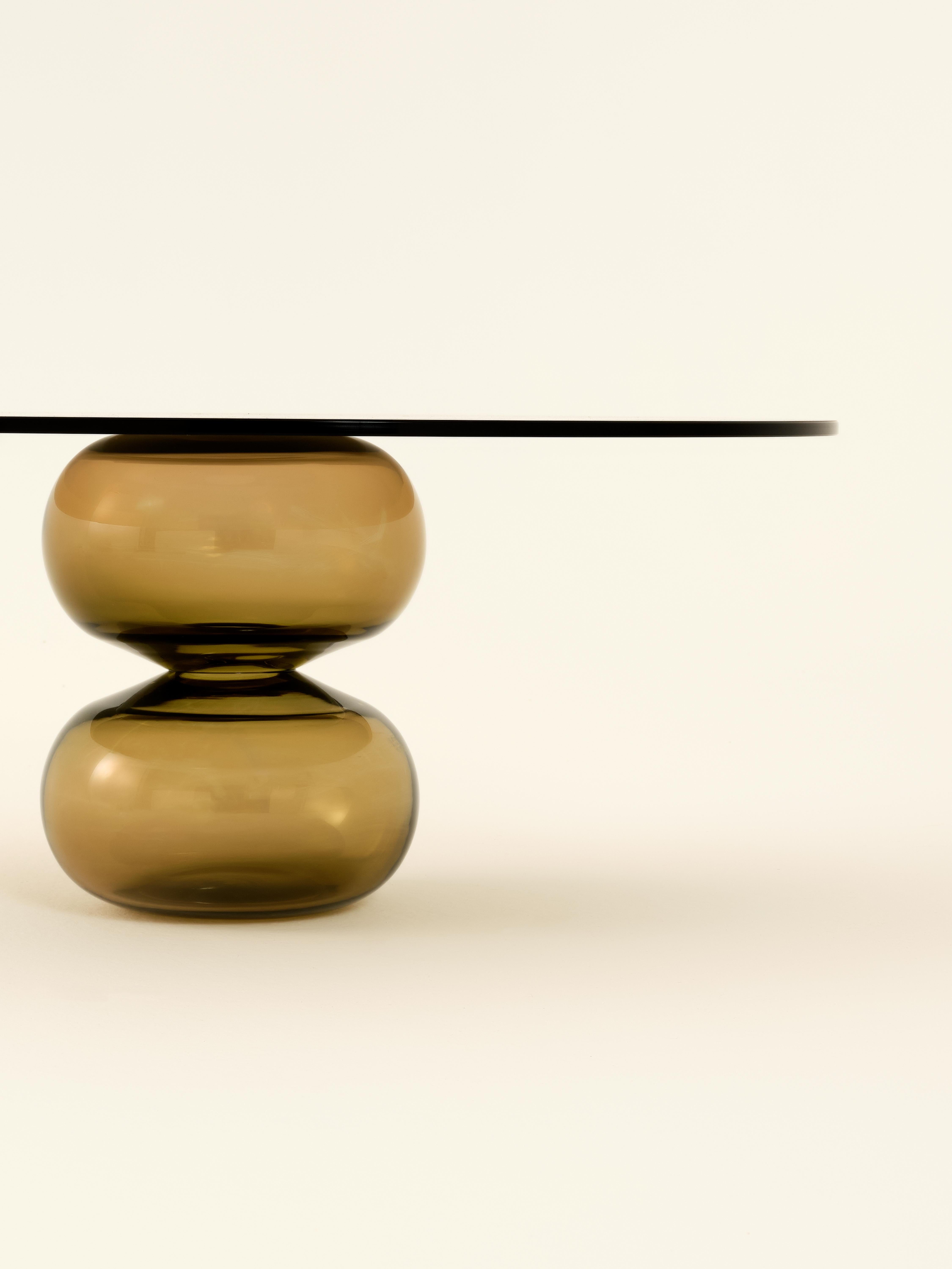 The Donut Coffee Table and Side Tables are thoughtfully designed with round bases crafted from mouth-blown glass, each showcasing subtle, unique variations that reflect the artistry of hand-blown techniques. The tops are made from tempered glass,