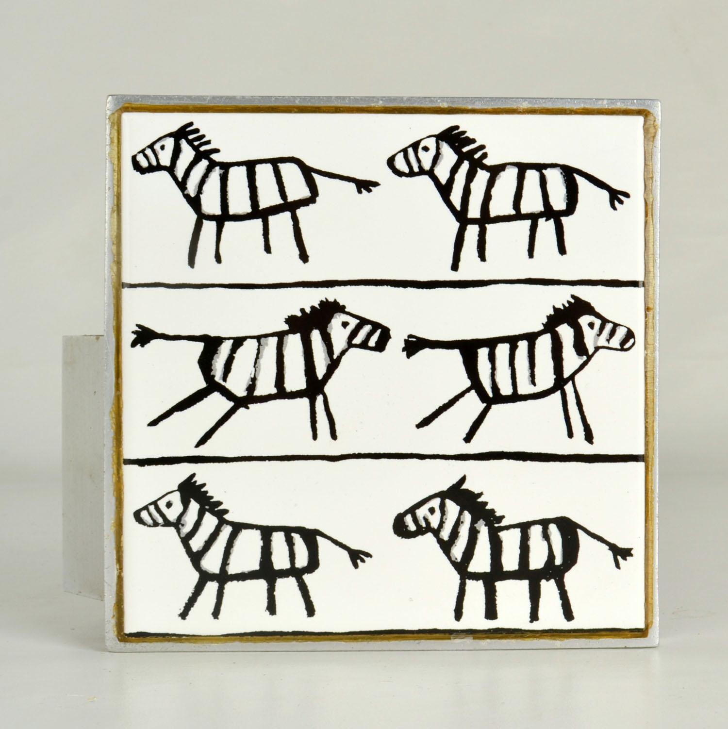 Manilla cuadrada simple de empujar y tirar, hecha con un azulejo de cerámica pintado a mano que representa cebras en esmalte blanco y negro, engastada en aluminio.
Las manillas se diseñaron en la década de 1960 para puertas de entrada. Son multiusos