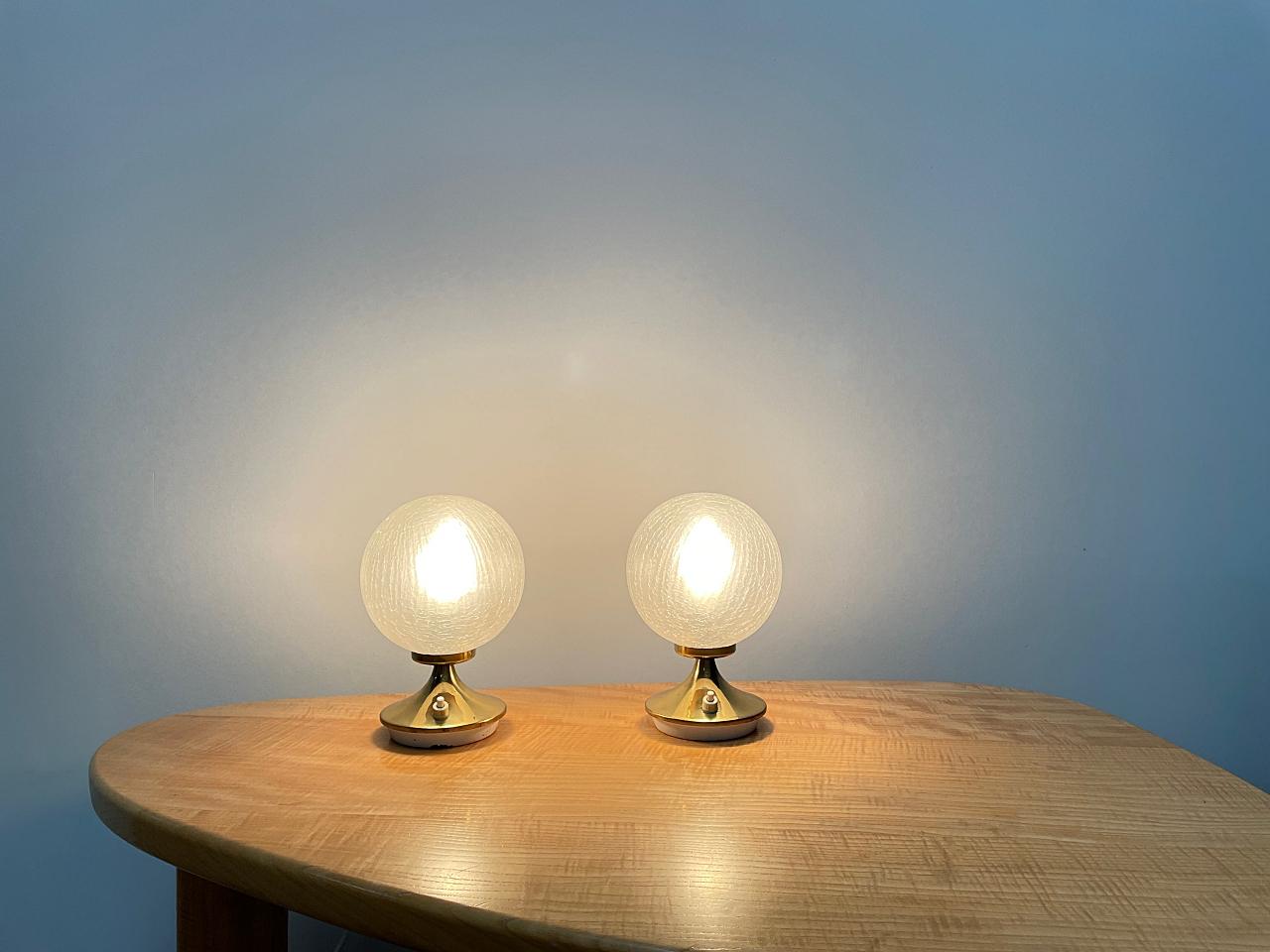 Elegant space age table, night stand lamps manufactured by DORIA Leuchten in Germany. The base is made of polished brass with mouth-blown crackle ice glass lampshades that provides smooth and wonderful light. The lamps are in good condition. 
Fully