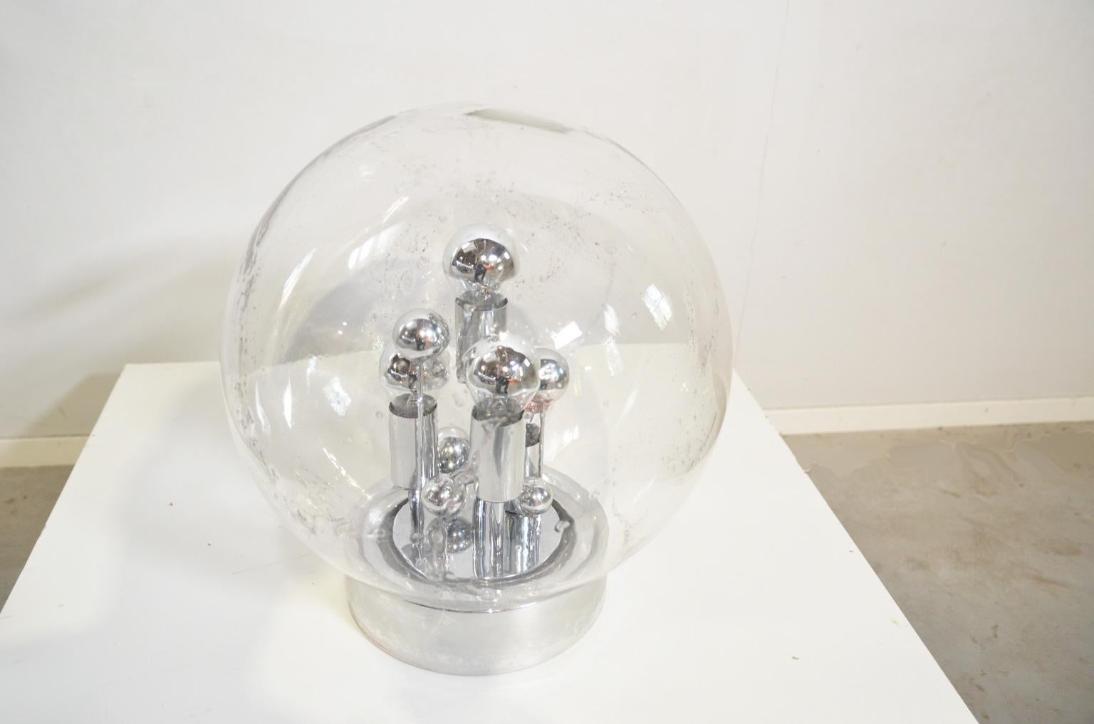 The 40 cm diameter hand blown sphere is resting on a chrome base which holds four lamp holders (E27) and some chromed spheres, all of various heights. The combination of the light bulbs, the chrome-plated spheres and the structure of the hand blown