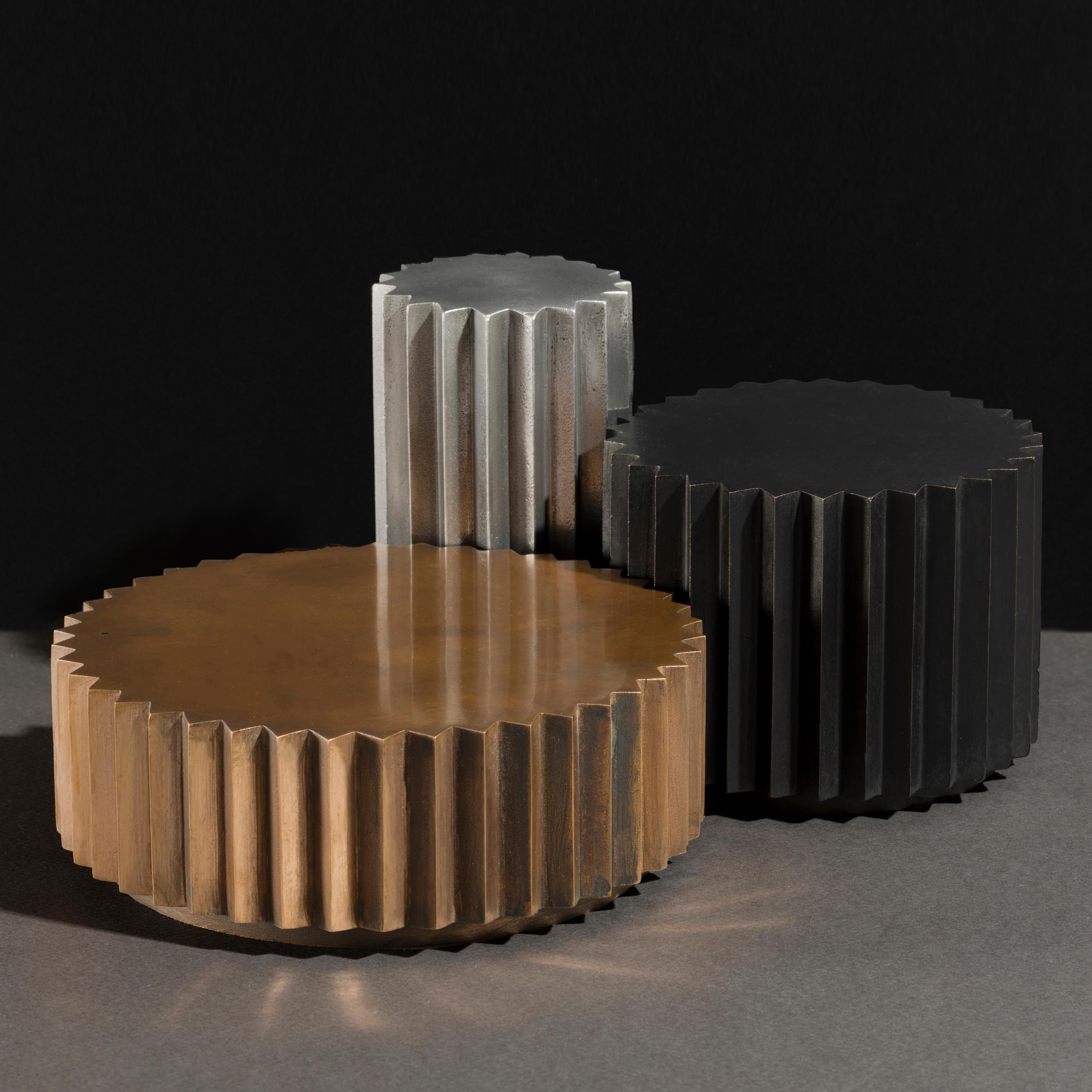 Side tables in cast bronze or aluminum of different diameters and heights that can be combined to create a coffee table. Inspired by Doric columns in archaic architecture, the extruded multi-point stars have a different finish on each vertical face: